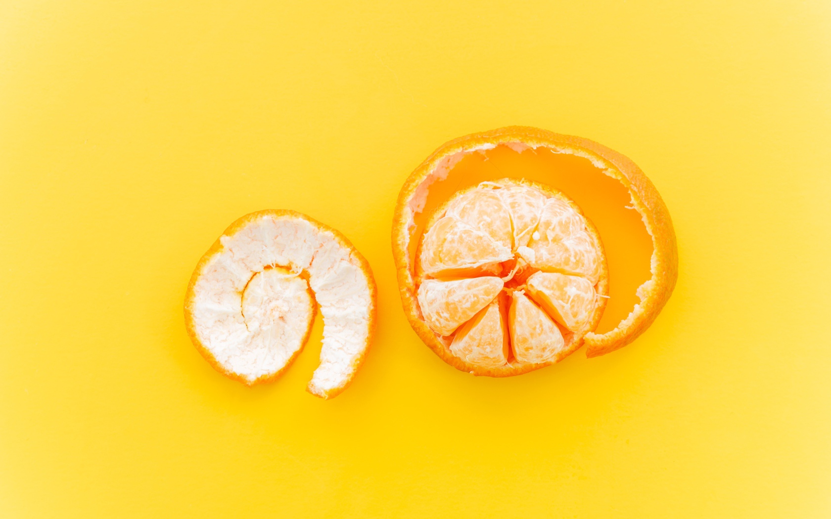 Очищенный мандарин с кожурой на желтом фоне 