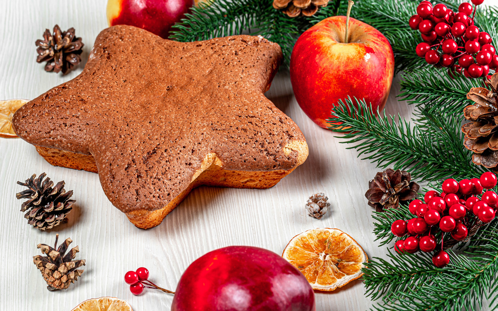 Рождественский кекс на столе с еловыми ветками,  яблоками и шишками