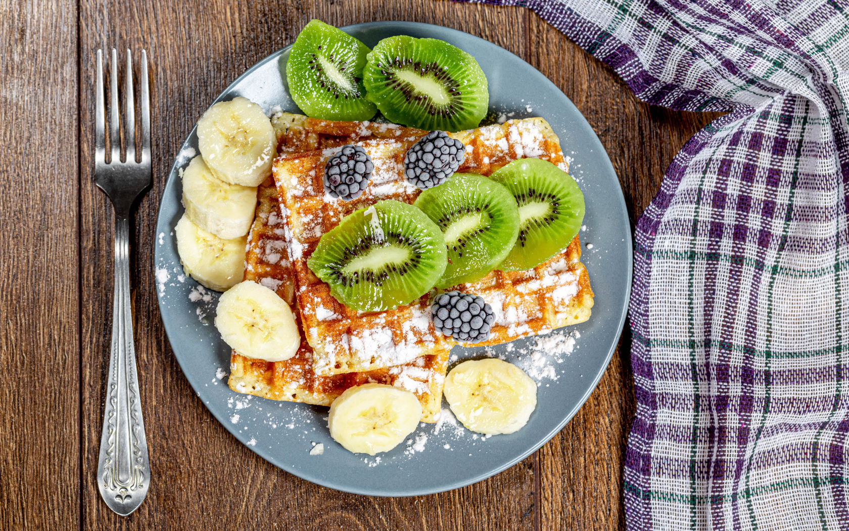 Сладкие вафли на тарелке с сахарной пудрой, бананами и киви