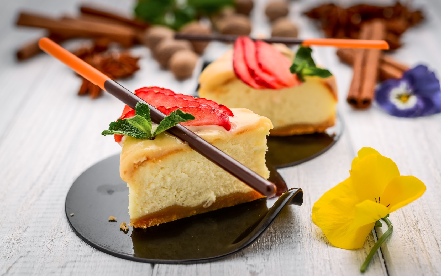 Два куска чизкейка с клубникой на столе с палочками