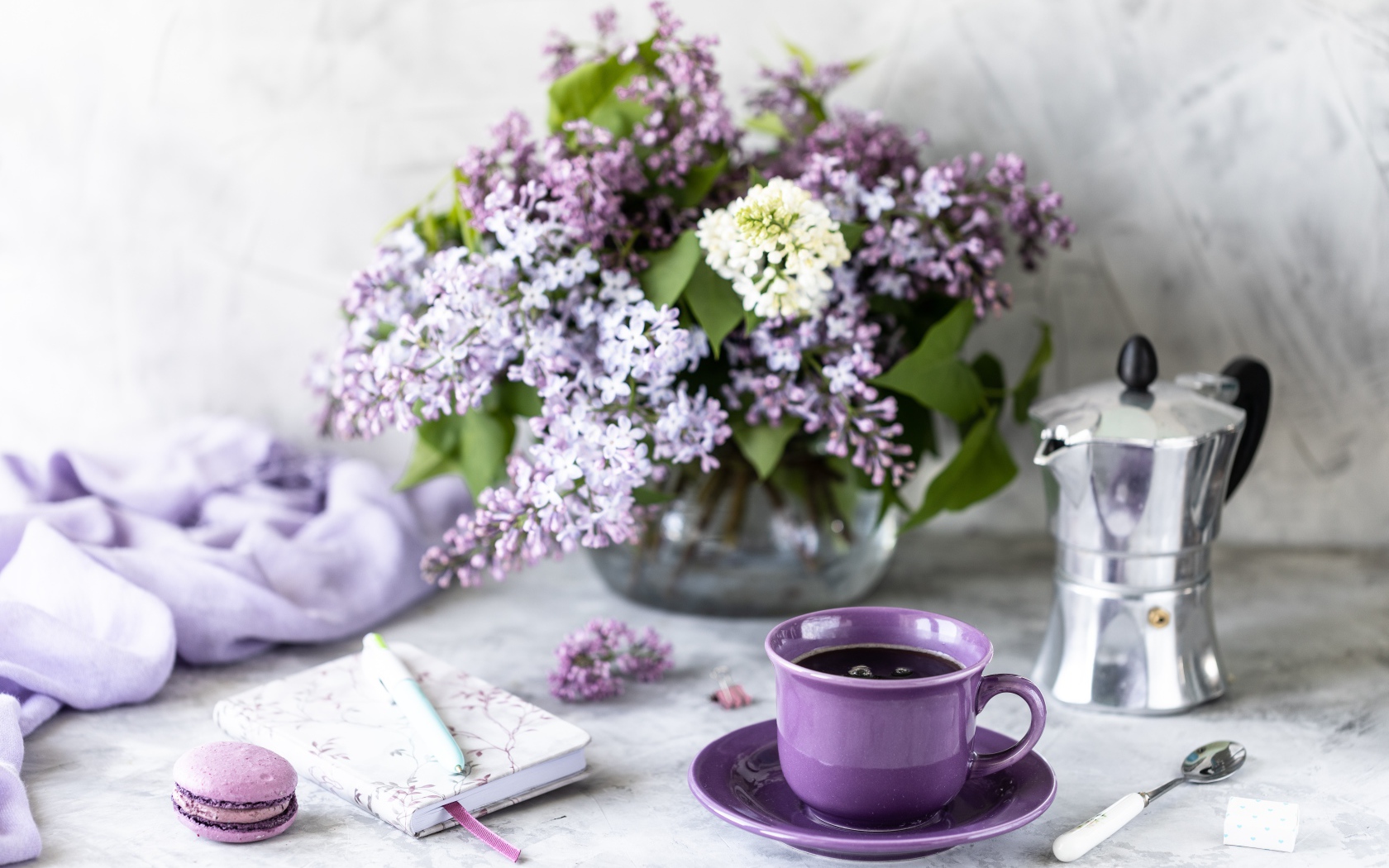 Чашка кофе на столе с блокнотом и букетом сирени в вазе