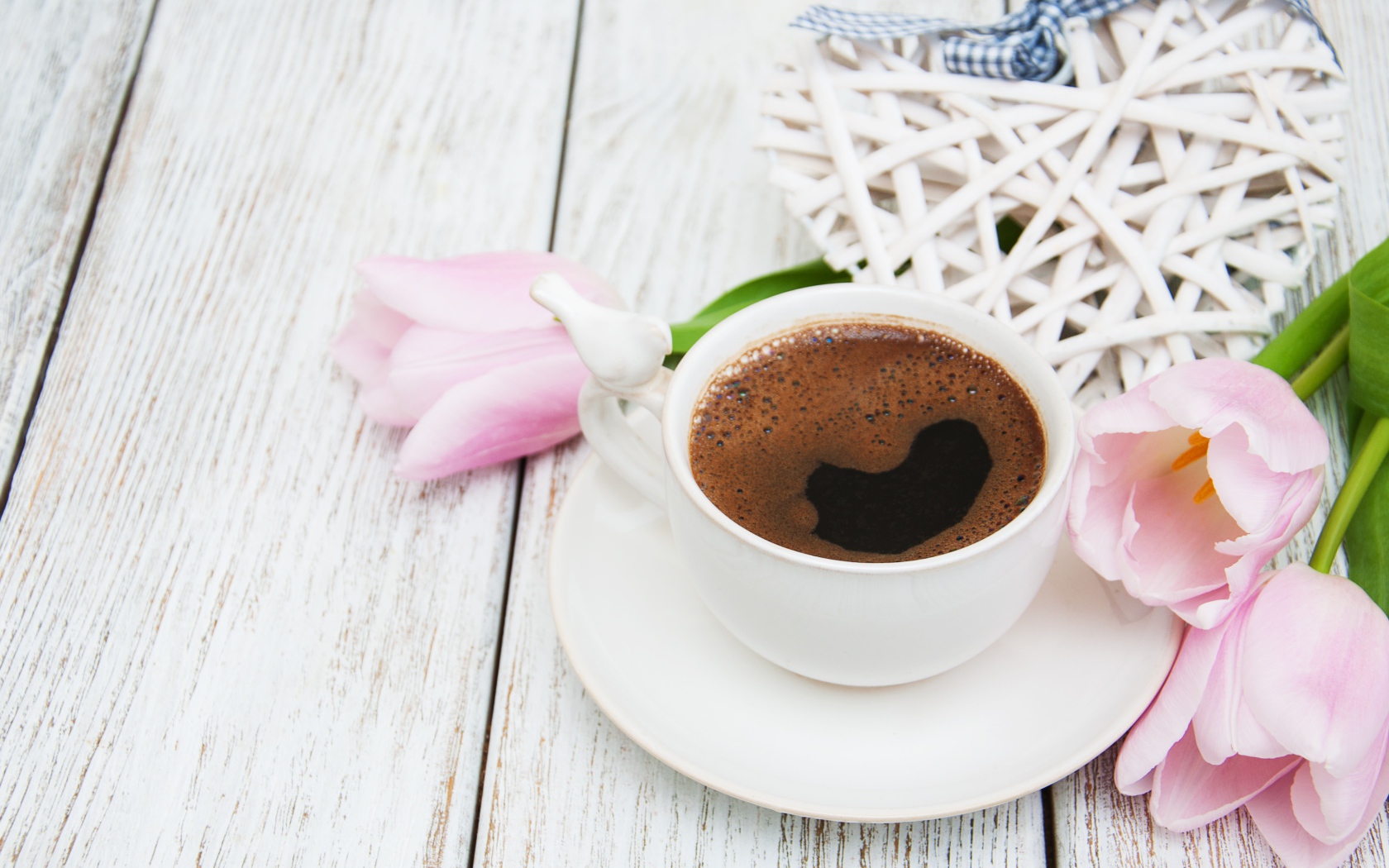 Чашка кофе на столе с розовыми тюльпанами и плетеным сердцем