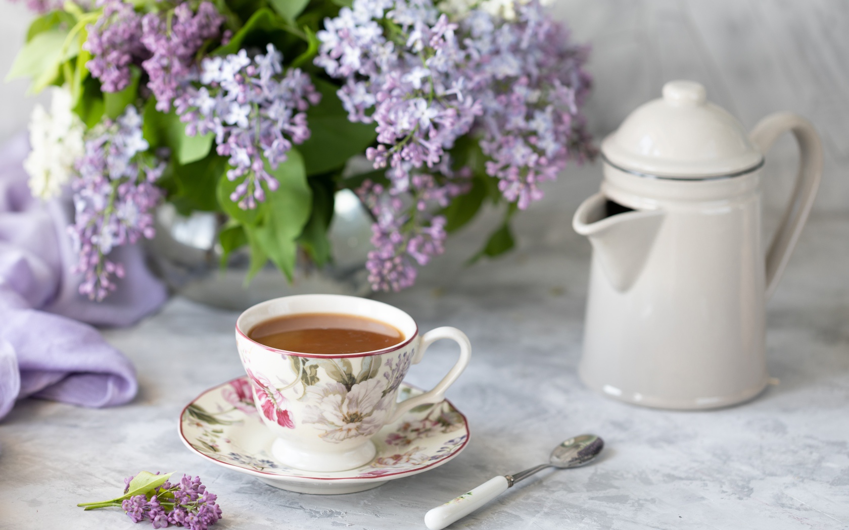 Чашка кофе с чайником на столе с букетом сирени 