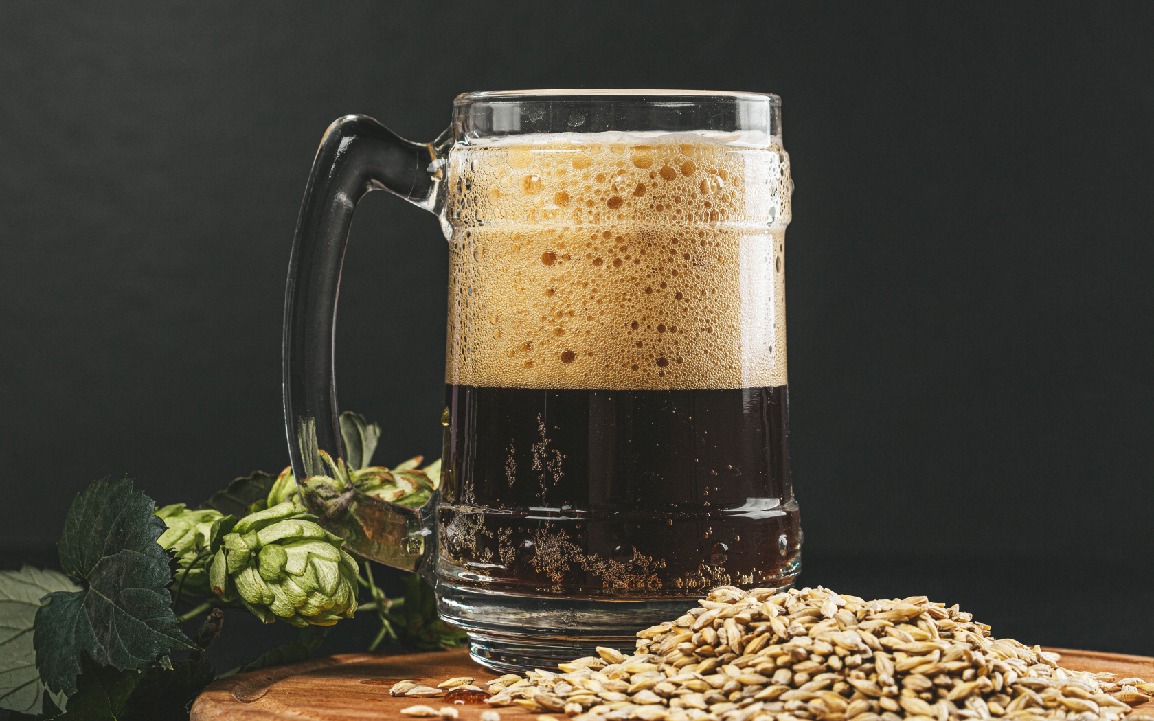 Темное пиво в бокале на столе с хмелем и зернами пшеницы 