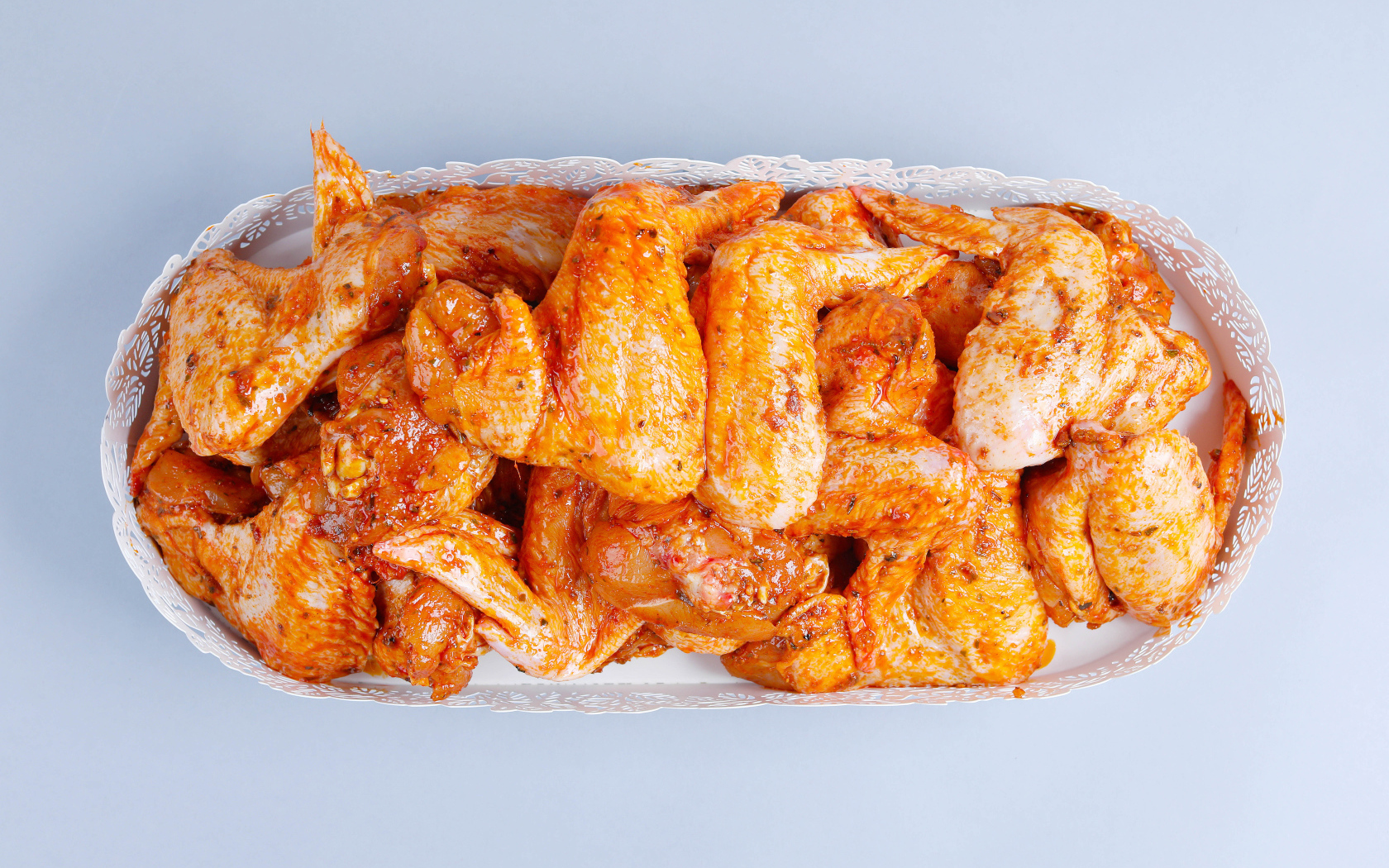 Жареные куриные крылья в белой корзине на сером фоне