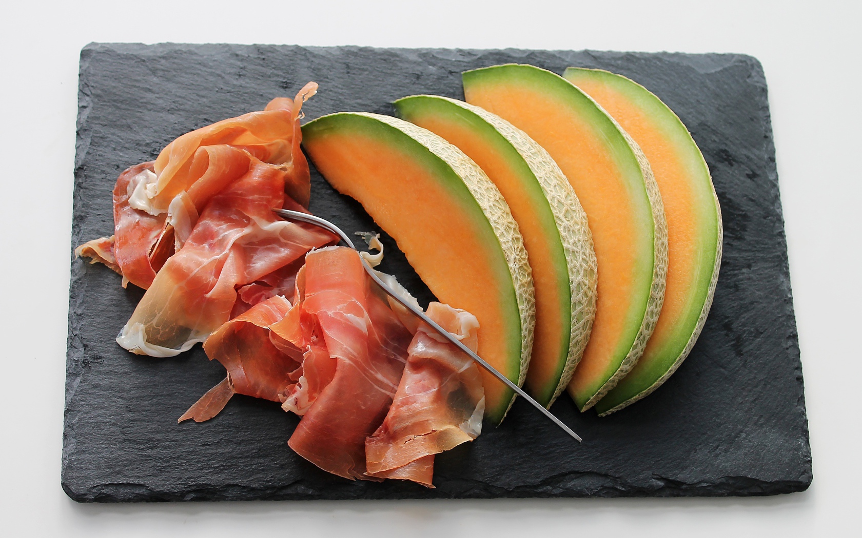 Кусочки дыни на доске с прошутто