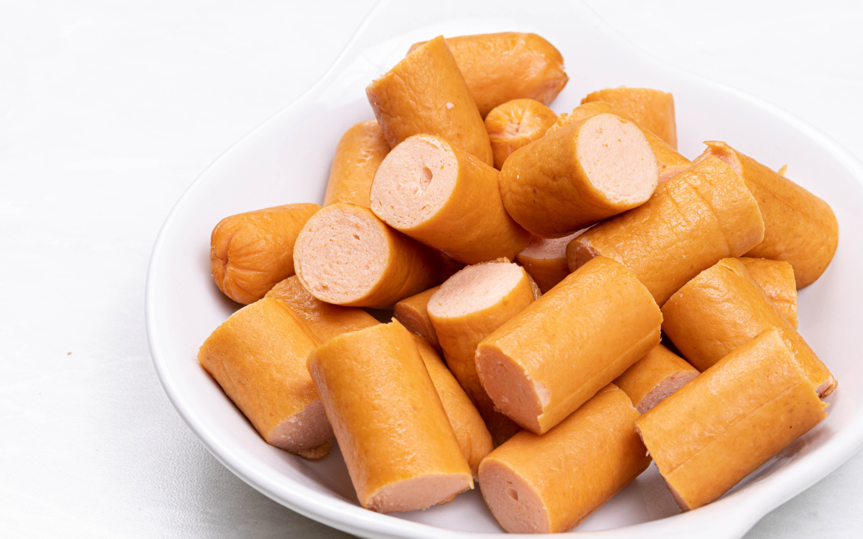 Молочные сосиски кусочками на белом фоне