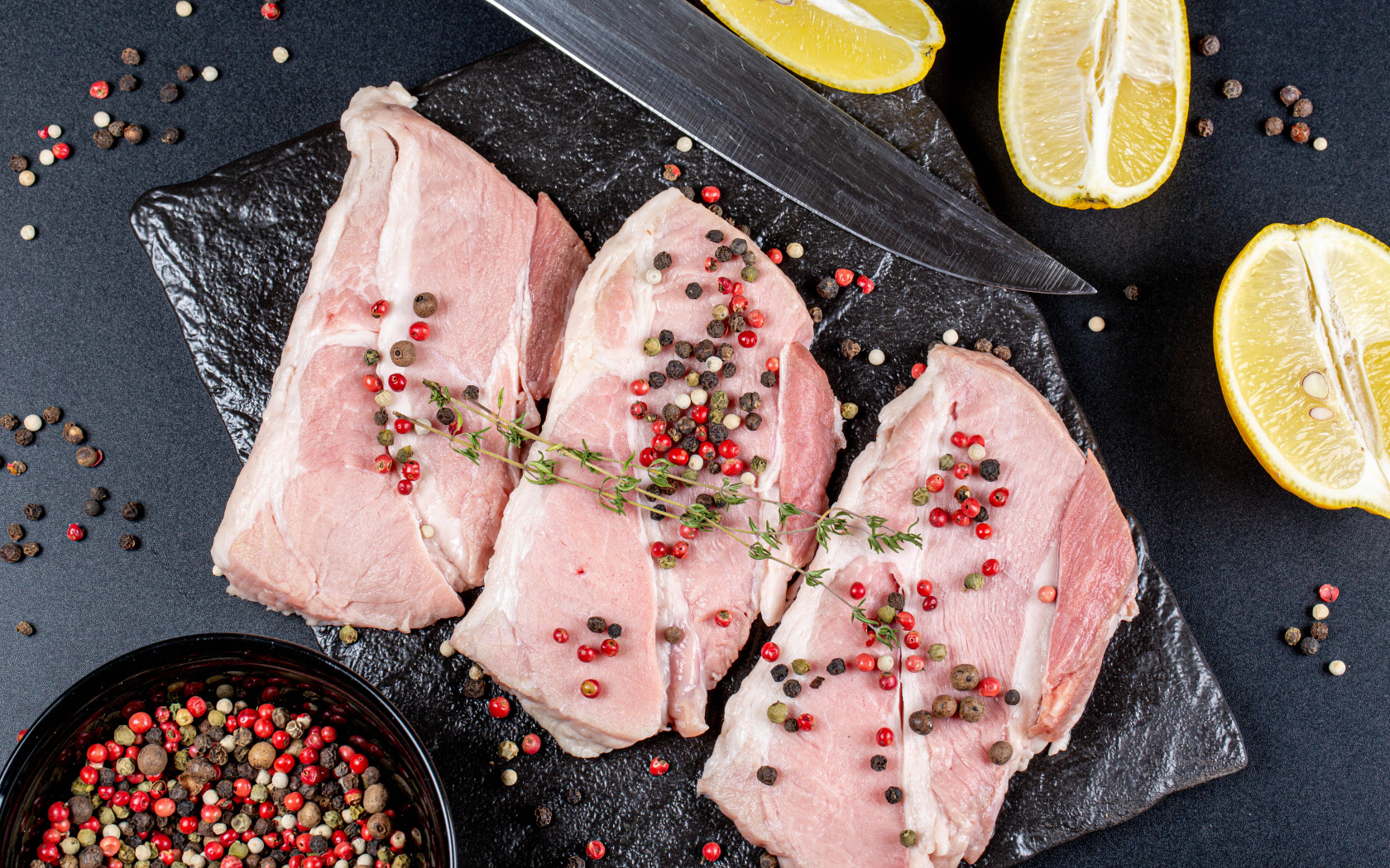 Куски свежего мяса на столе с зернами перца и лимоном