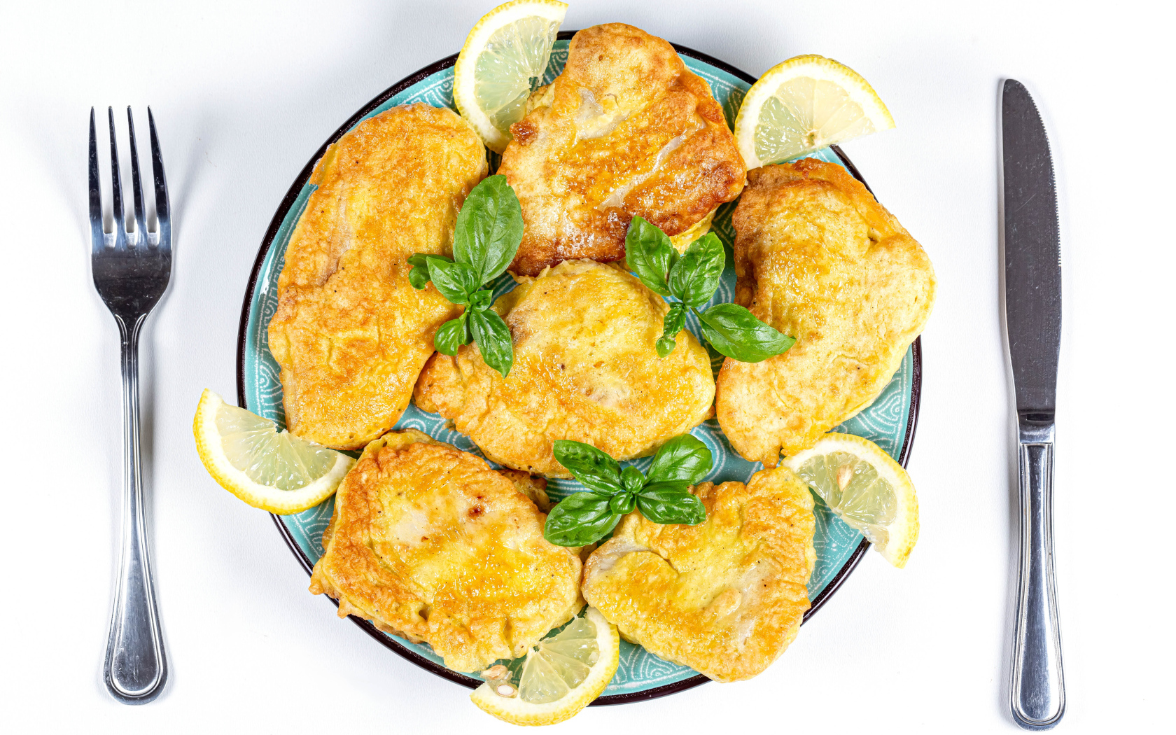 Appetizing fish in batter on a plate with lemon slices and cutlery