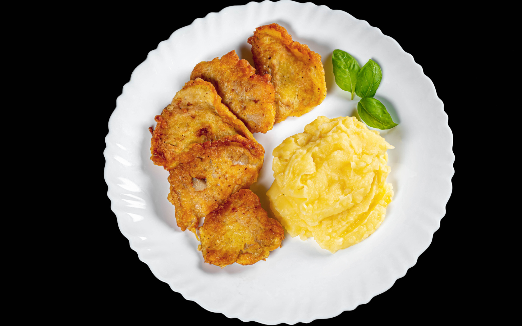 Куски жареной рыбы с картофельным пюре в тарелке на черном фоне