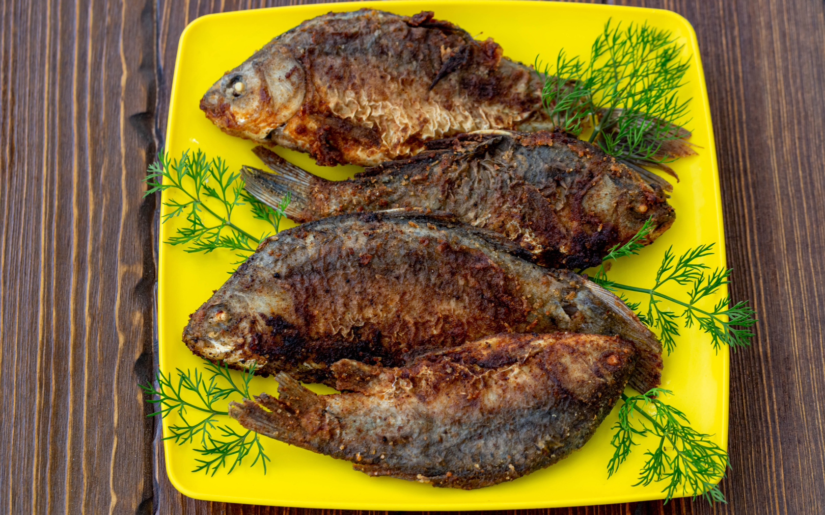 Жареные караси с укропом на желтой тарелке 