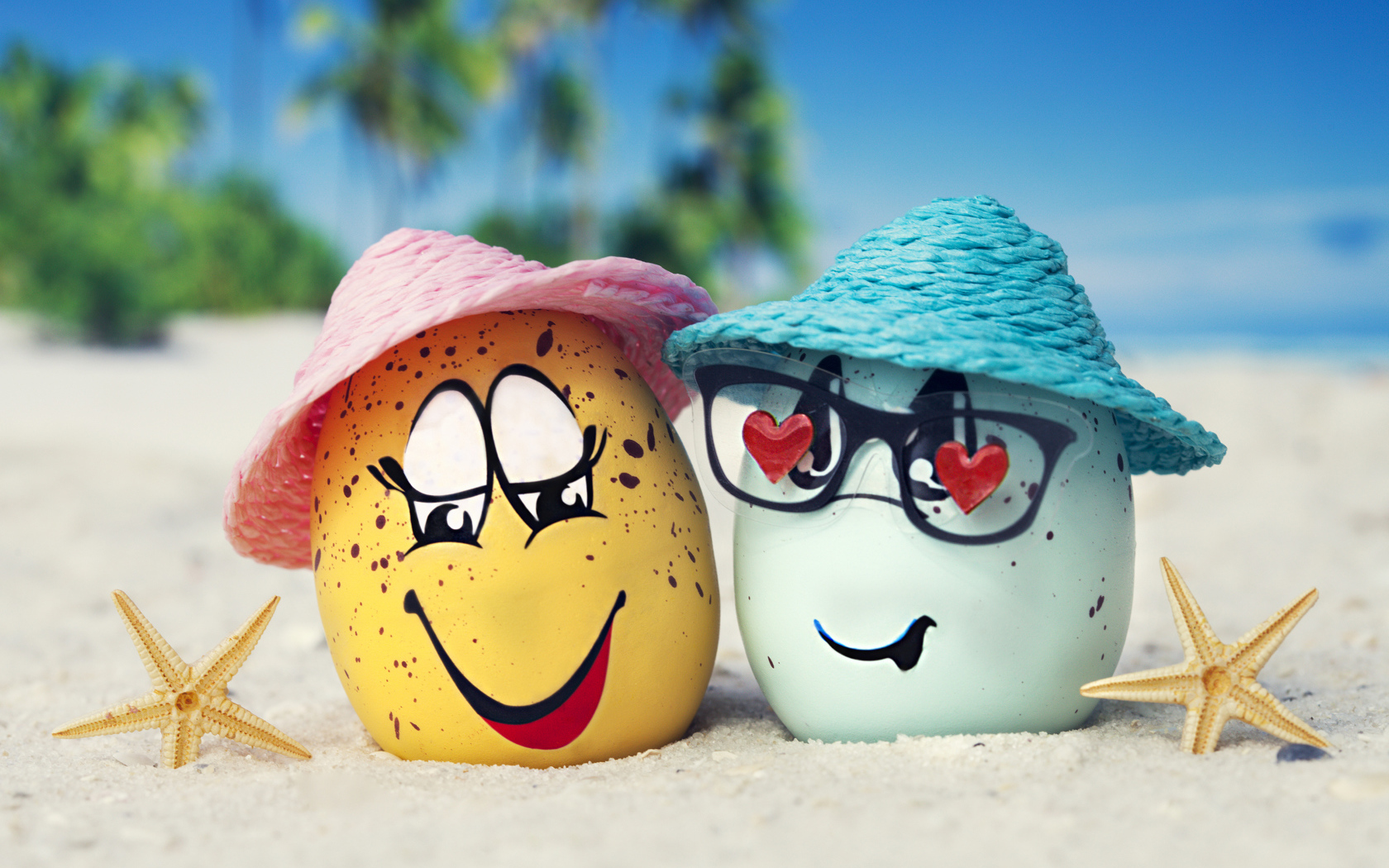 Two eggs in hats on the sand with starfish in summer