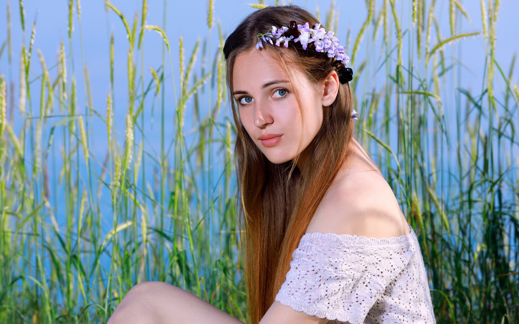 Красивая молодая девушка с венком на голове сидит на поле с колосьями 