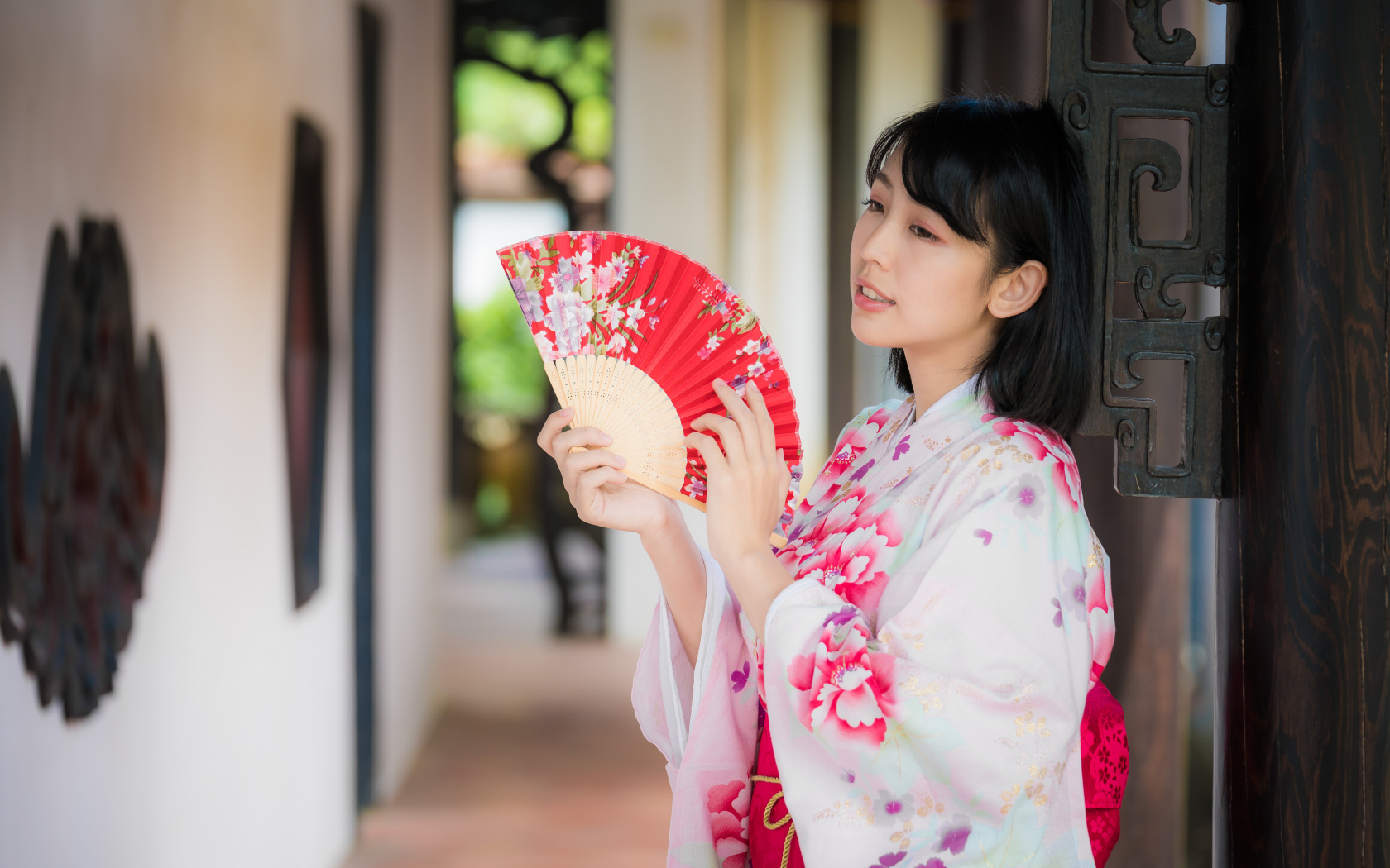 Девушка азиатка в кимоно с веером в руке стоит у ворот 