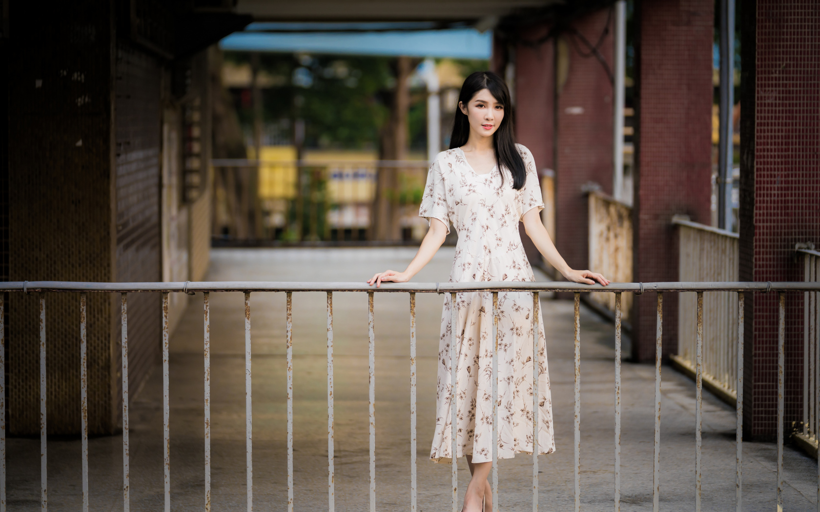 Красивая азиатка в платье стоит у перил