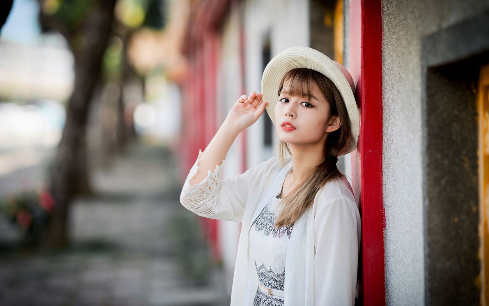 Красивая азиатка в шляпе стоит у стены