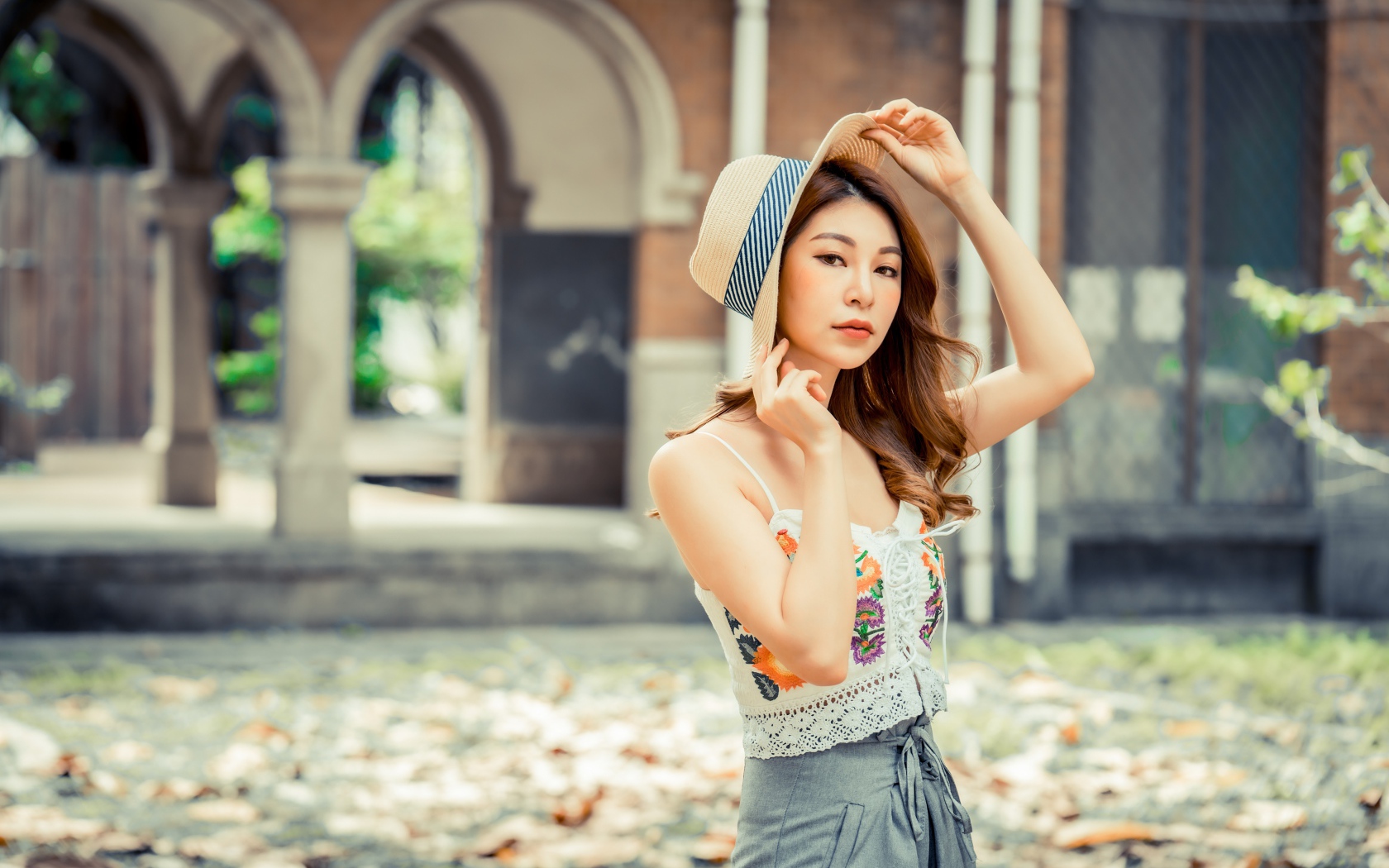 Красивая девушка азиатка в шляпе стоит в парке 