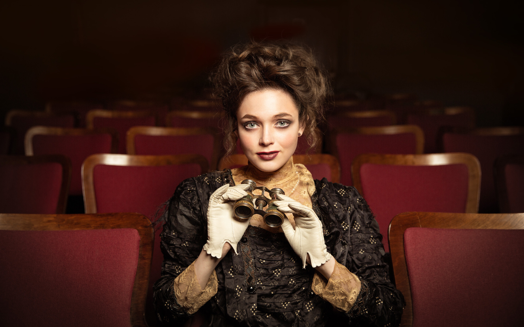 Красивая девушка с биноклем сидит в театре