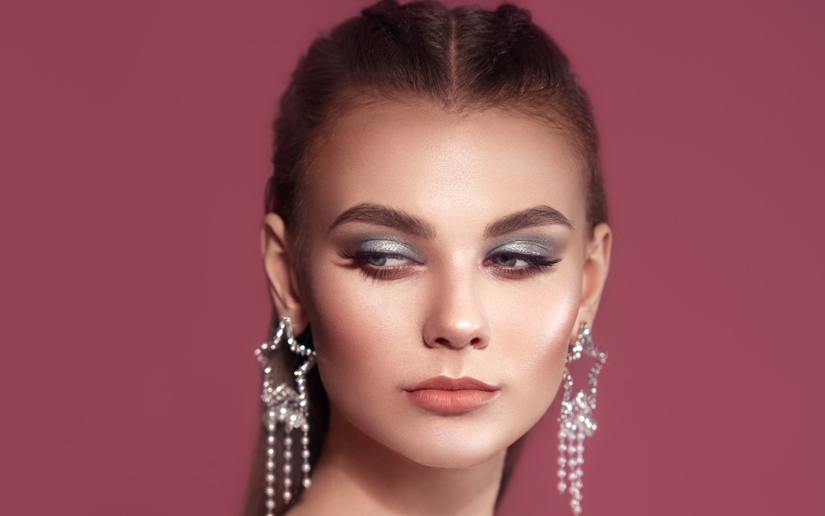 Красивая девушка с макияжем и большими серьгами на розовом фоне