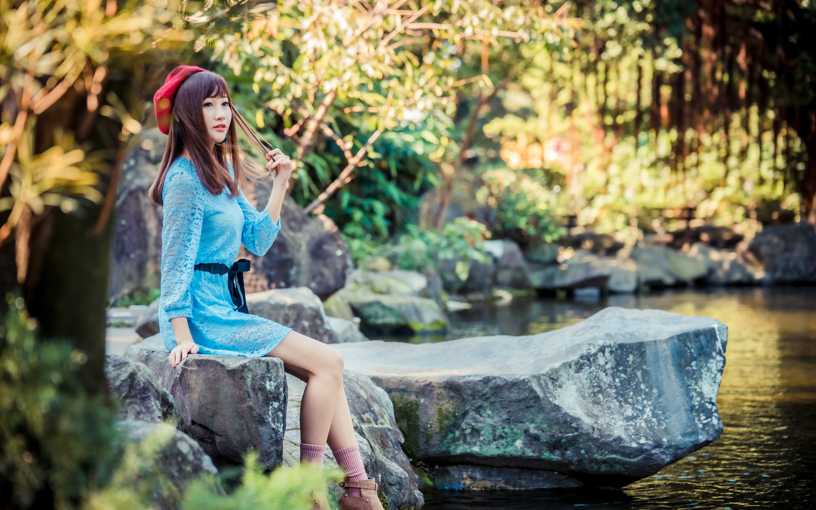 Милая азиатка в берете и синем платье сидит у воды 
