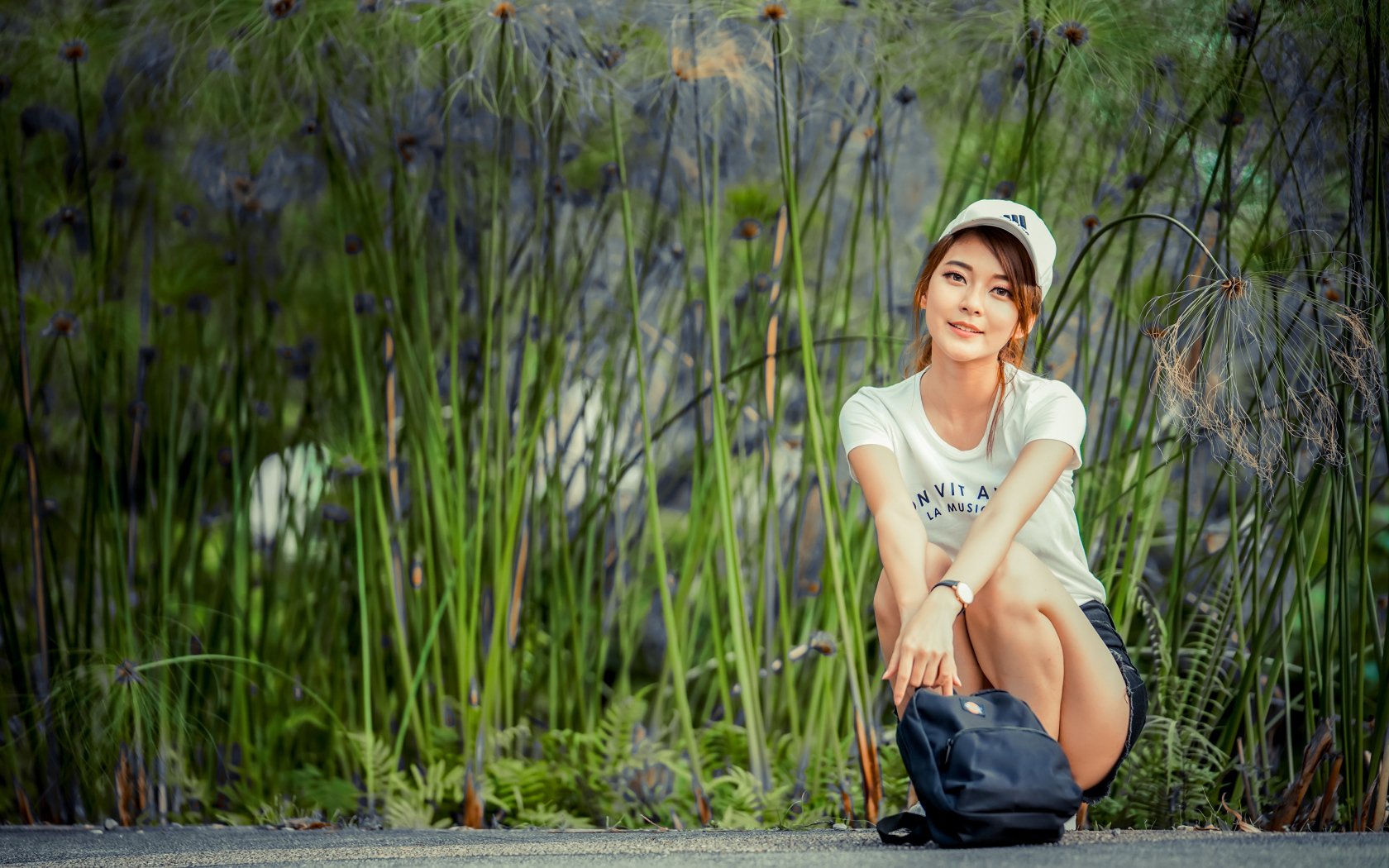 Милая девушка в кепке сидит на дороге с рюкзаком