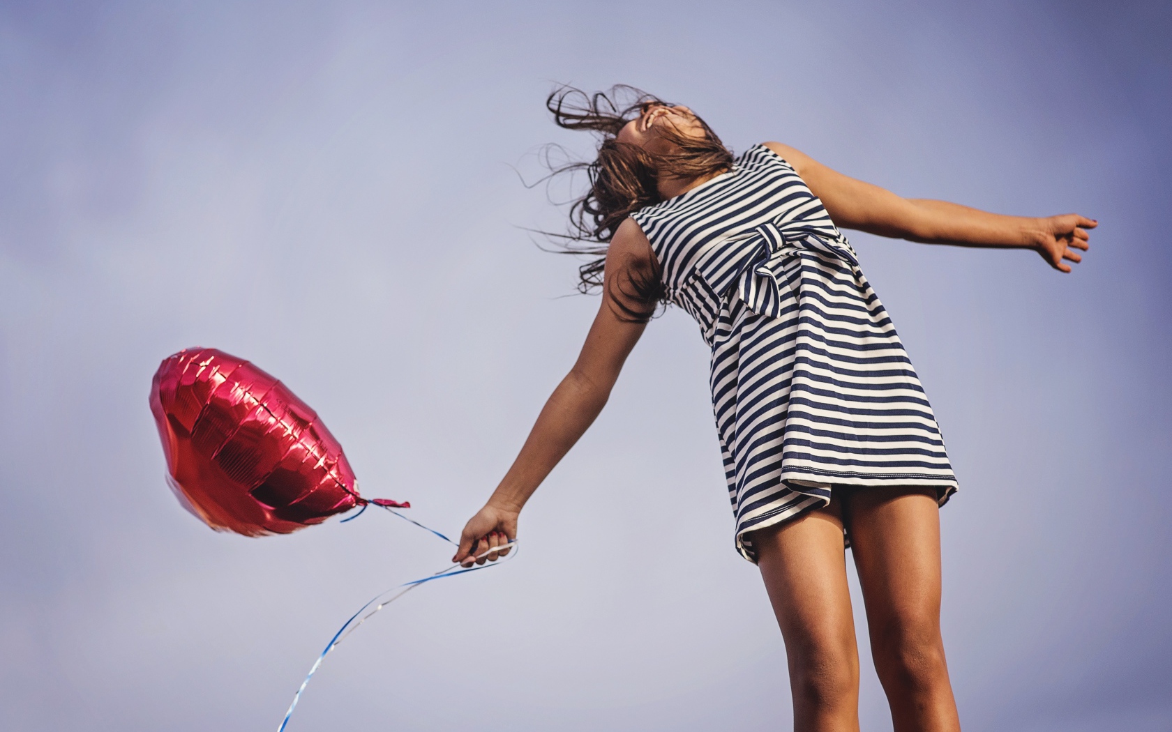 Девушка в полосатом платье прыгает с шариком 