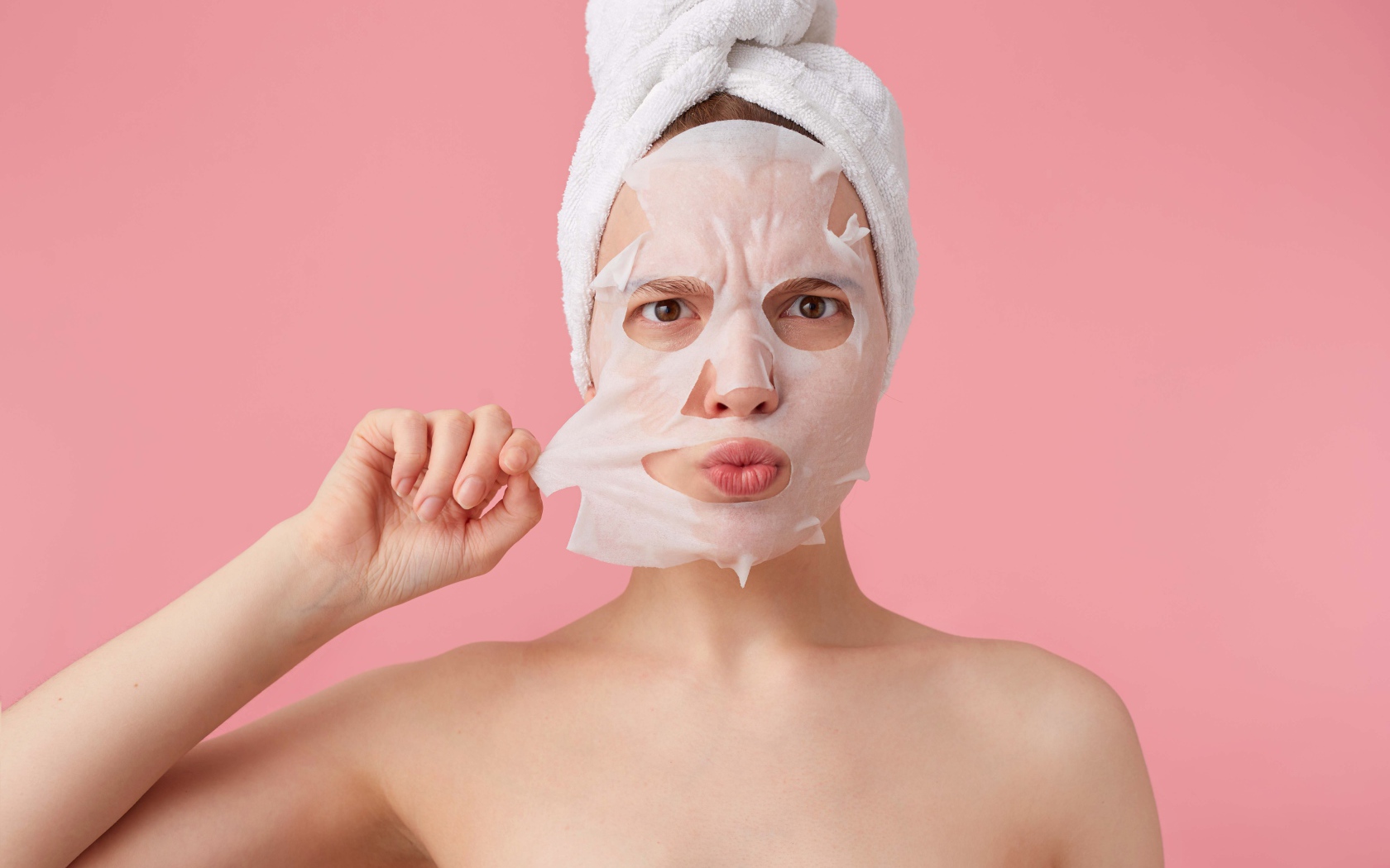 Девушка снимает косметическую маску с лица на розовом фоне 