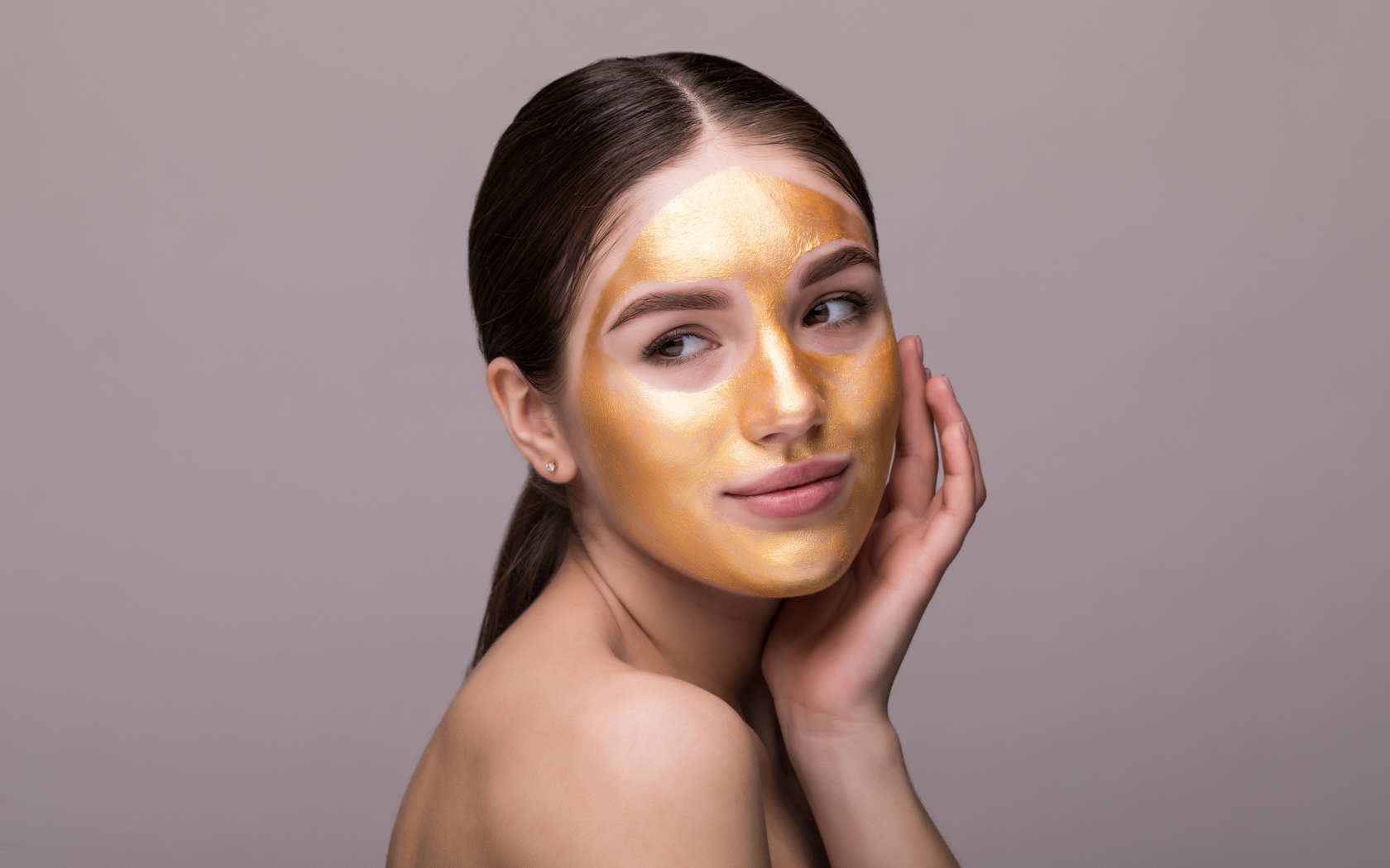 Золотая маска на лице у молодой девушки 