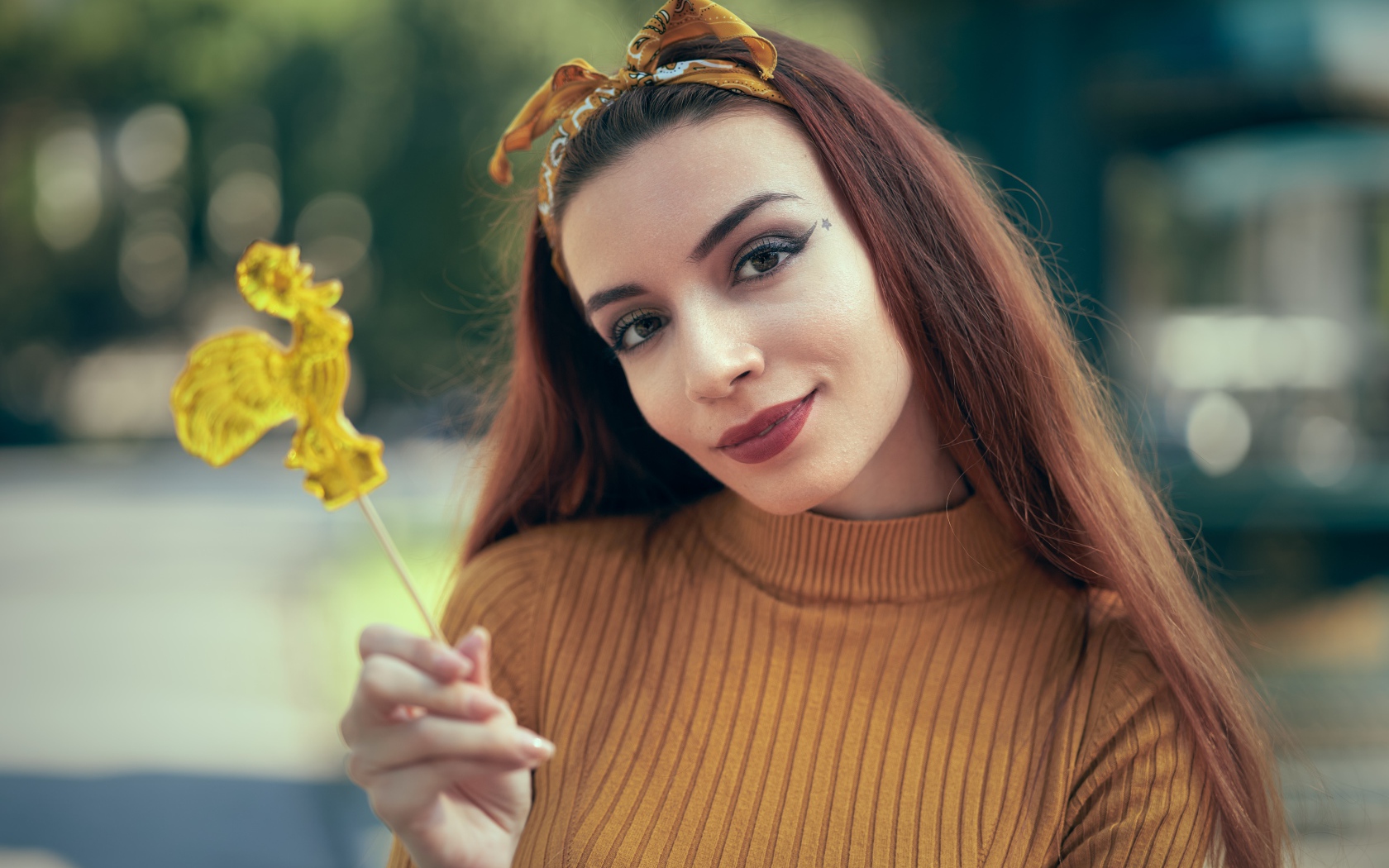 Длинноволосая девушка в свитере с леденцом в руке