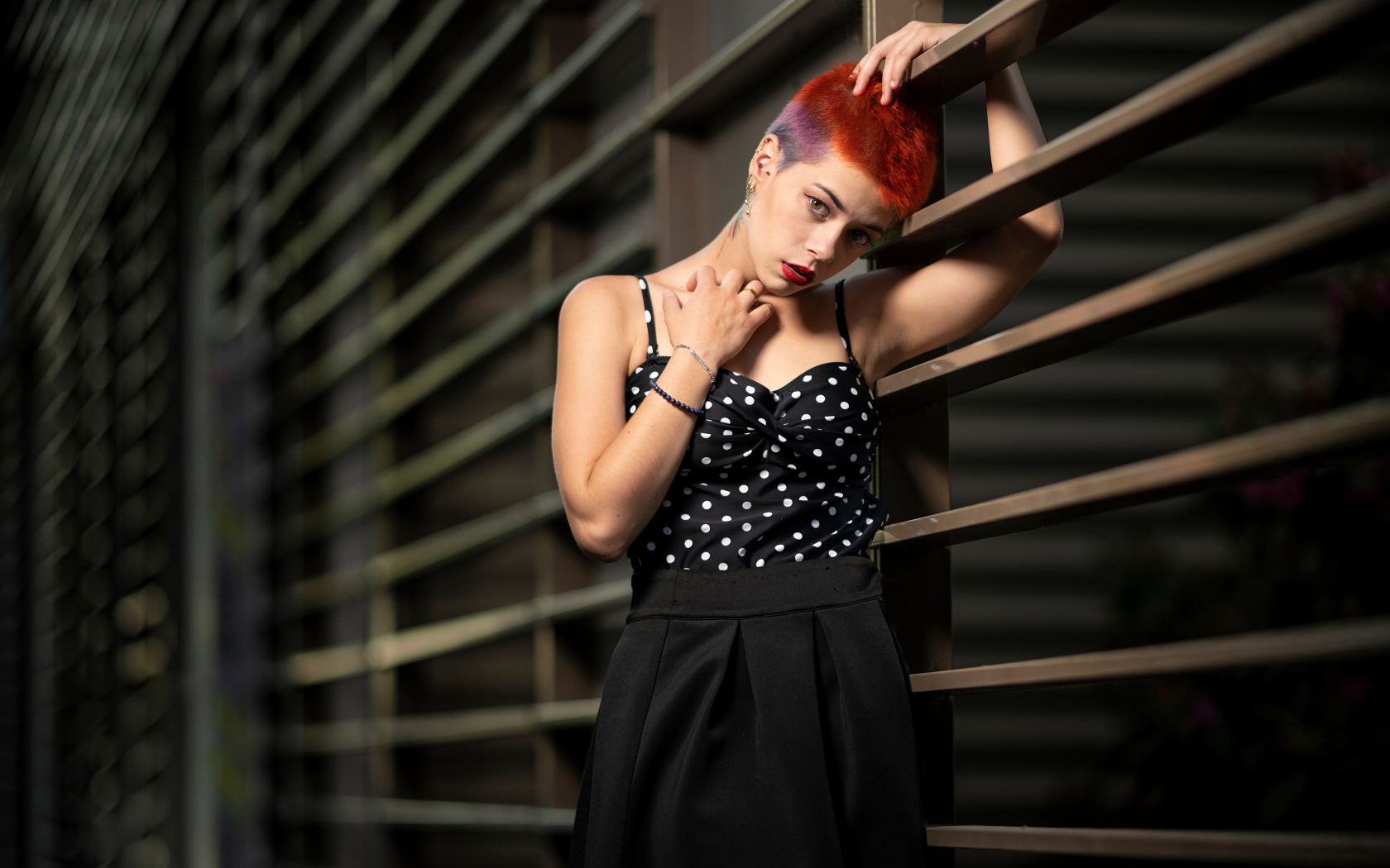 Эпатажная девушка с короткой стрижкой стоит у забора 