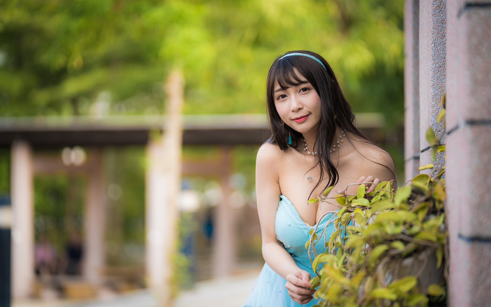 Улыбающаяся девушка азиатка в голубом платье у стены с растением 