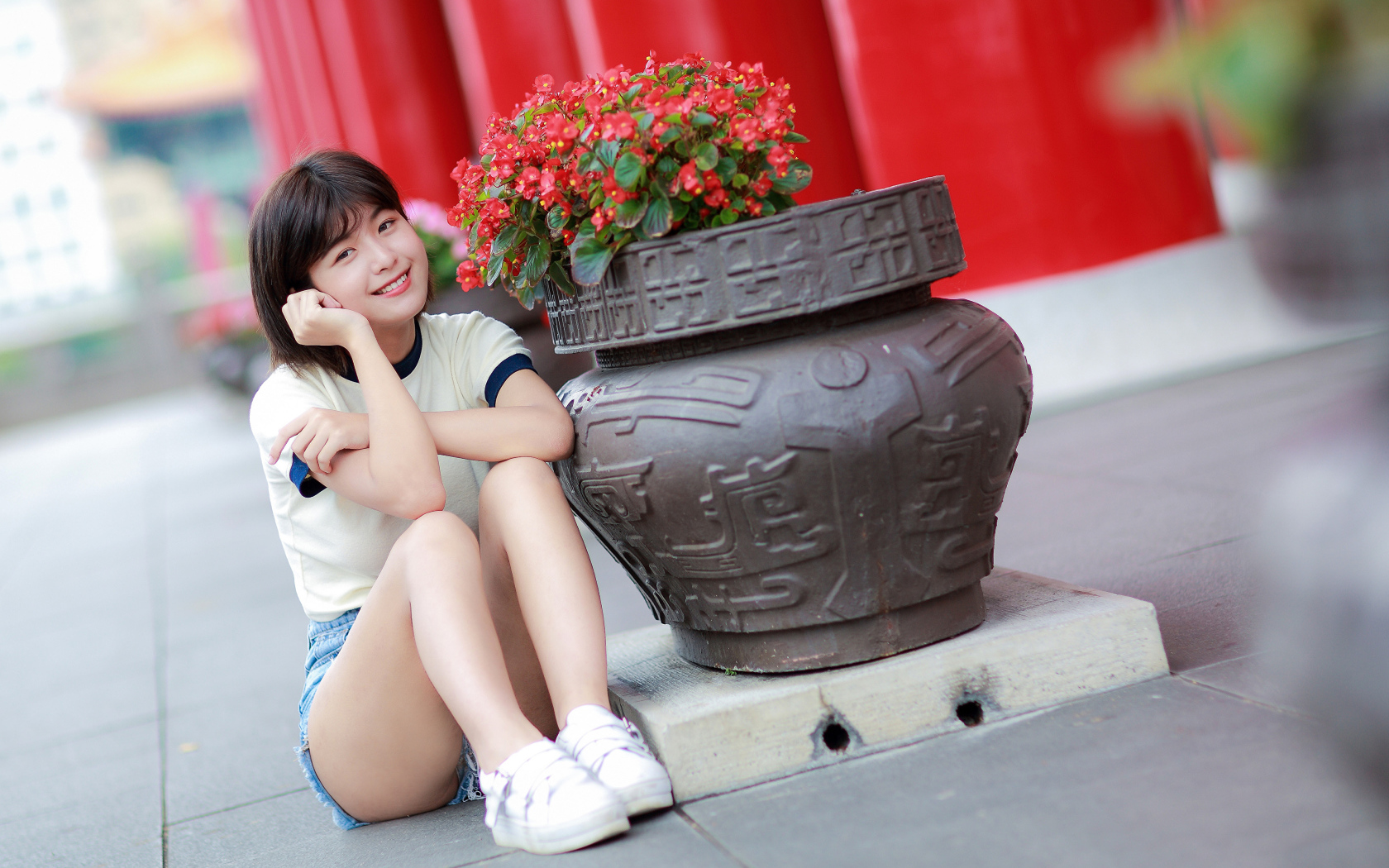 Улыбающаяся азиатка сидит у клумбы с цветами