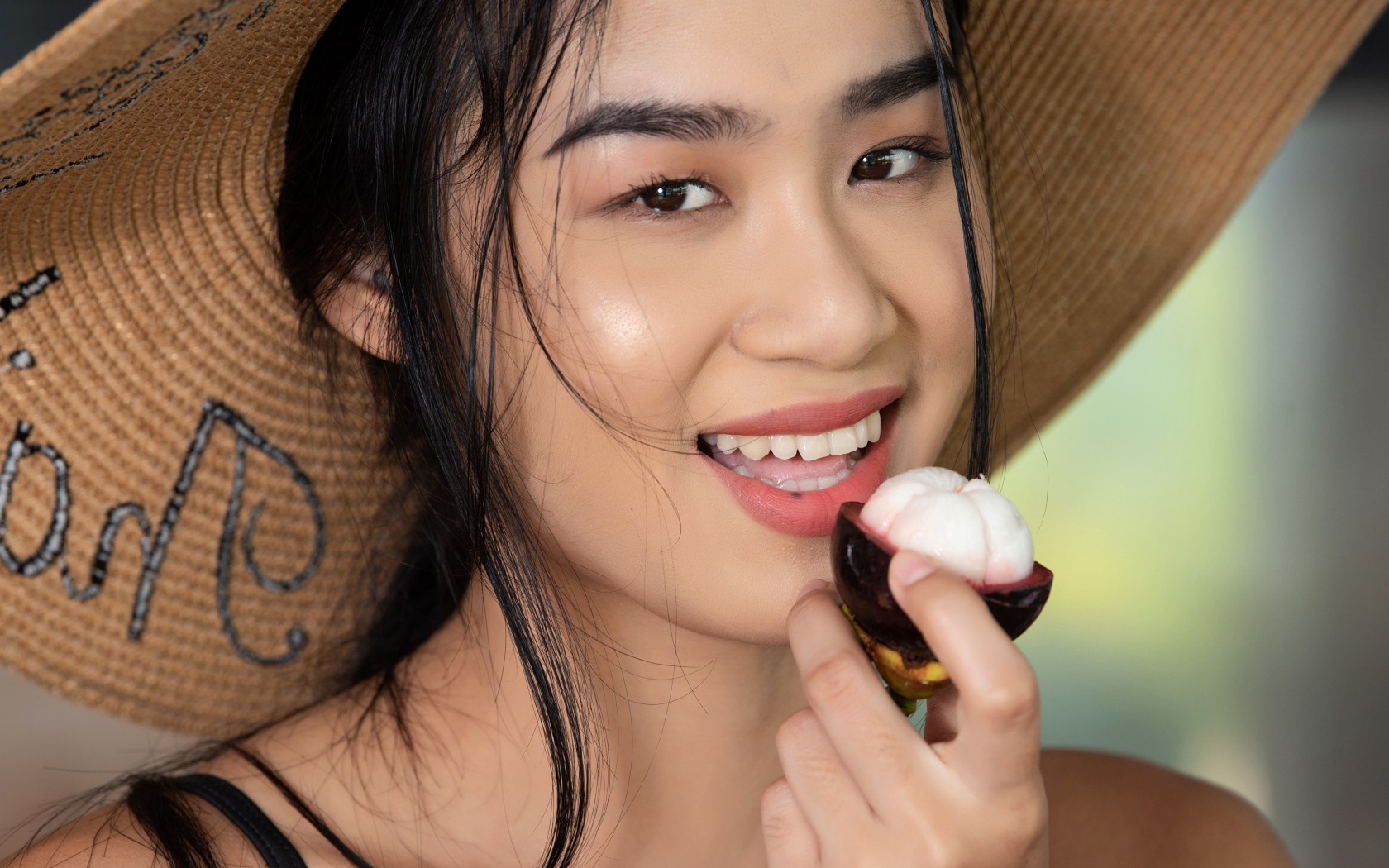 Улыбающаяся азиатка в шляпе с фруктом в руке