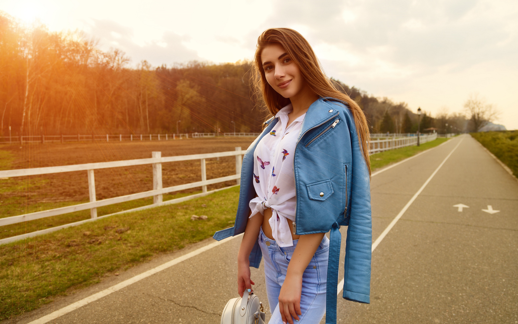 Улыбающаяся девушка в синей кожаной куртке на дороге 