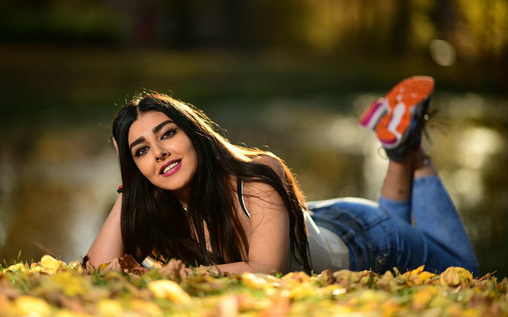 Улыбающаяся девушка модель лежит на земле с опавшими листьями