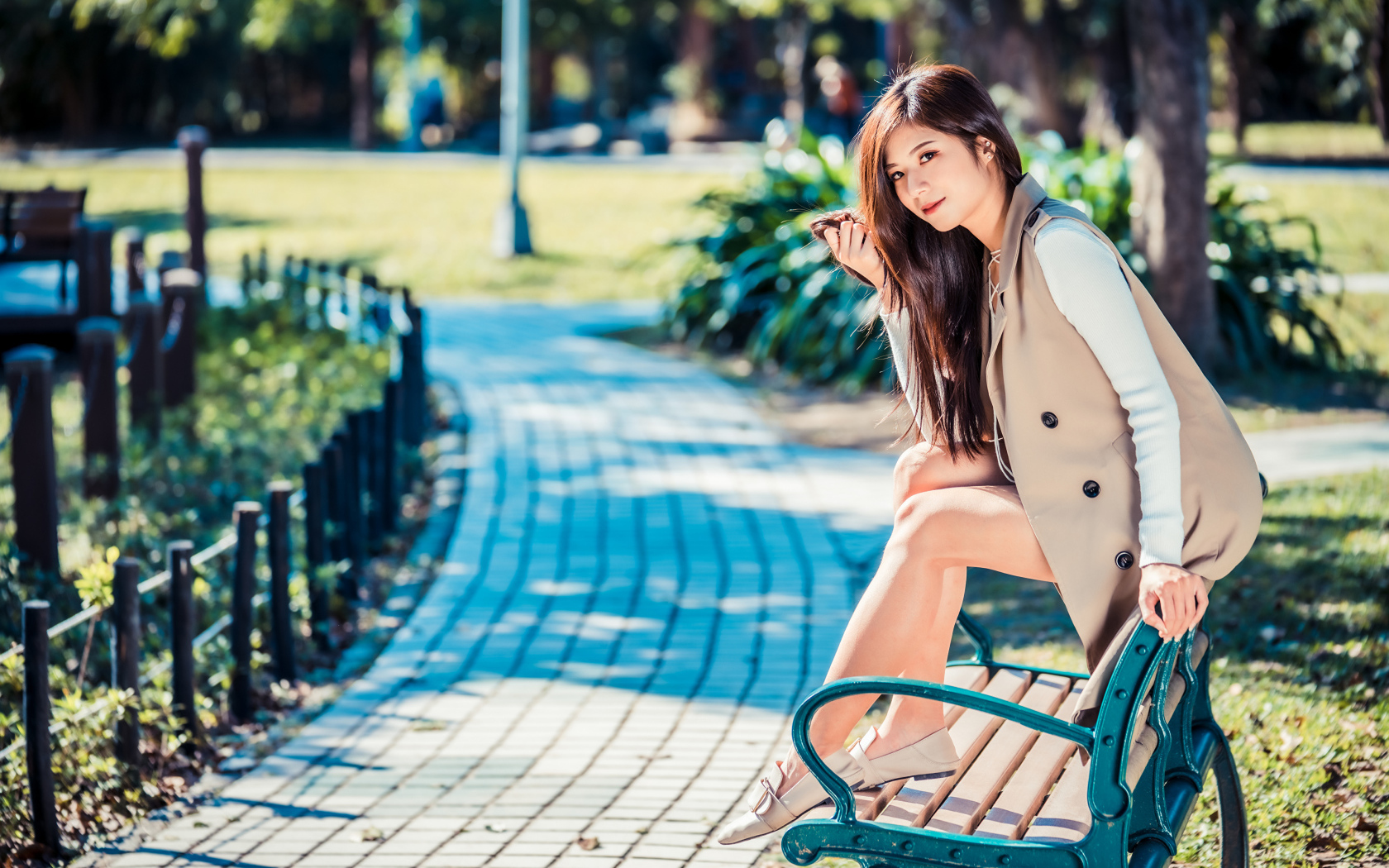 Молодая девушка азиатка сидит в пальто на лавке в парке 