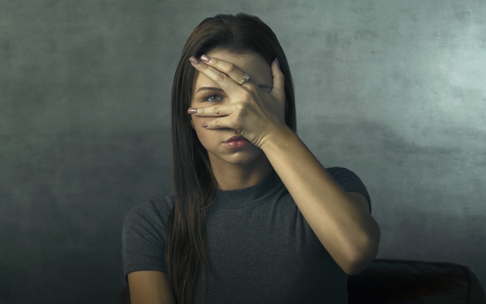 Молодая девушка закрыла лицо рукой на сером фоне