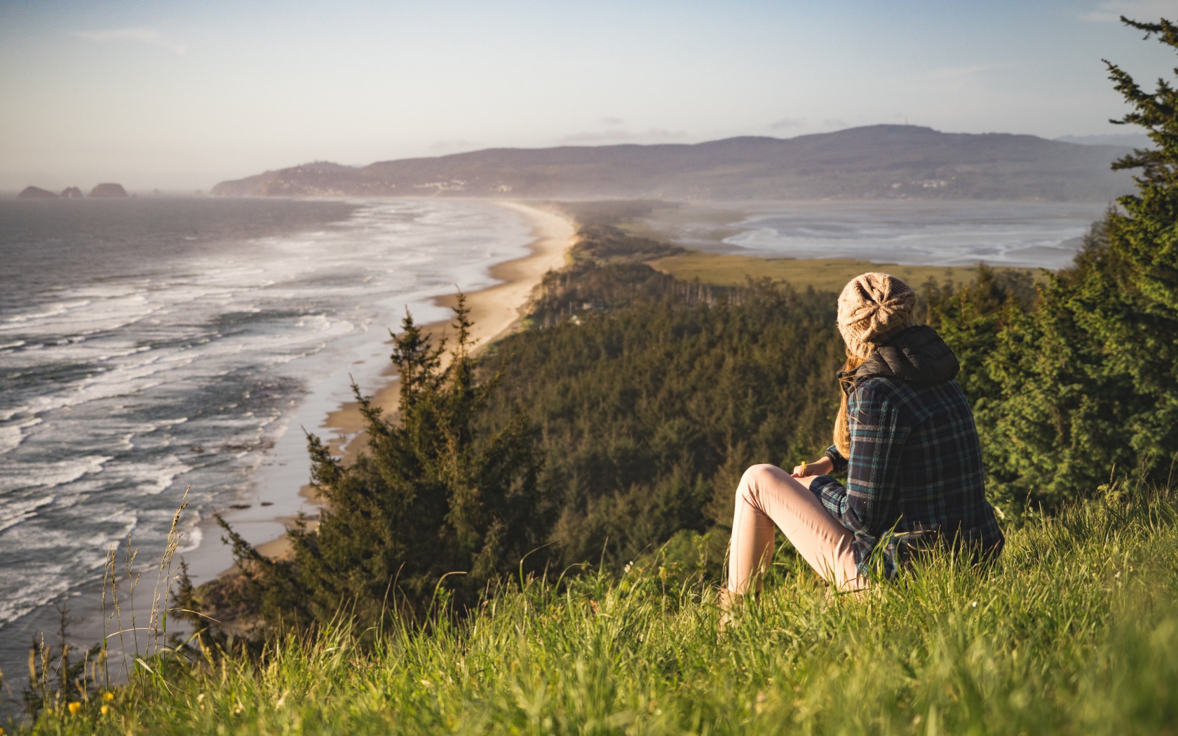 Молодая девушка сидит на зеленой траве на фоне моря