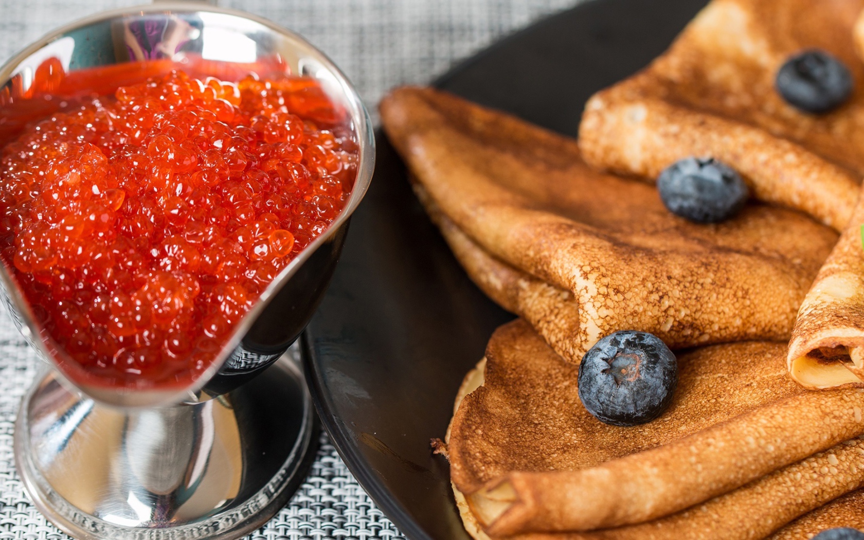 Тонкие блины с ягодами черники на столе с красной икрой на Масленицу