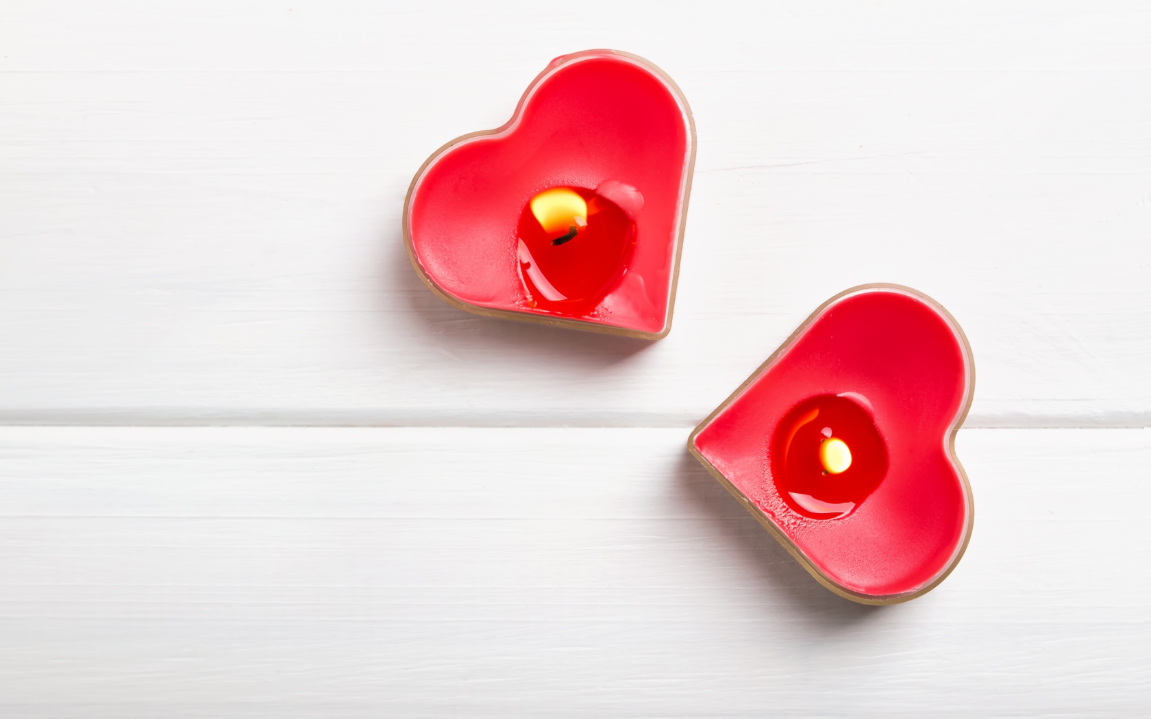 Две зажженные свечи в форме сердца на столе 