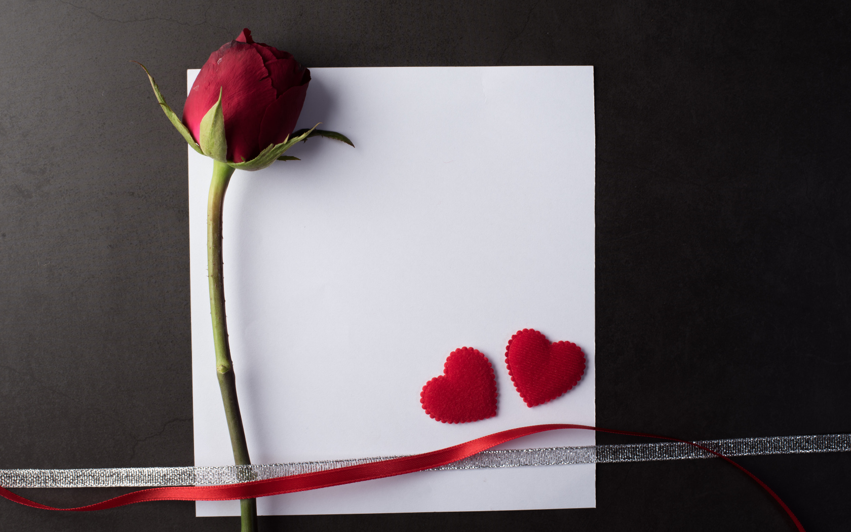 Белый лист бумаги, роза и ленточки на сером фоне