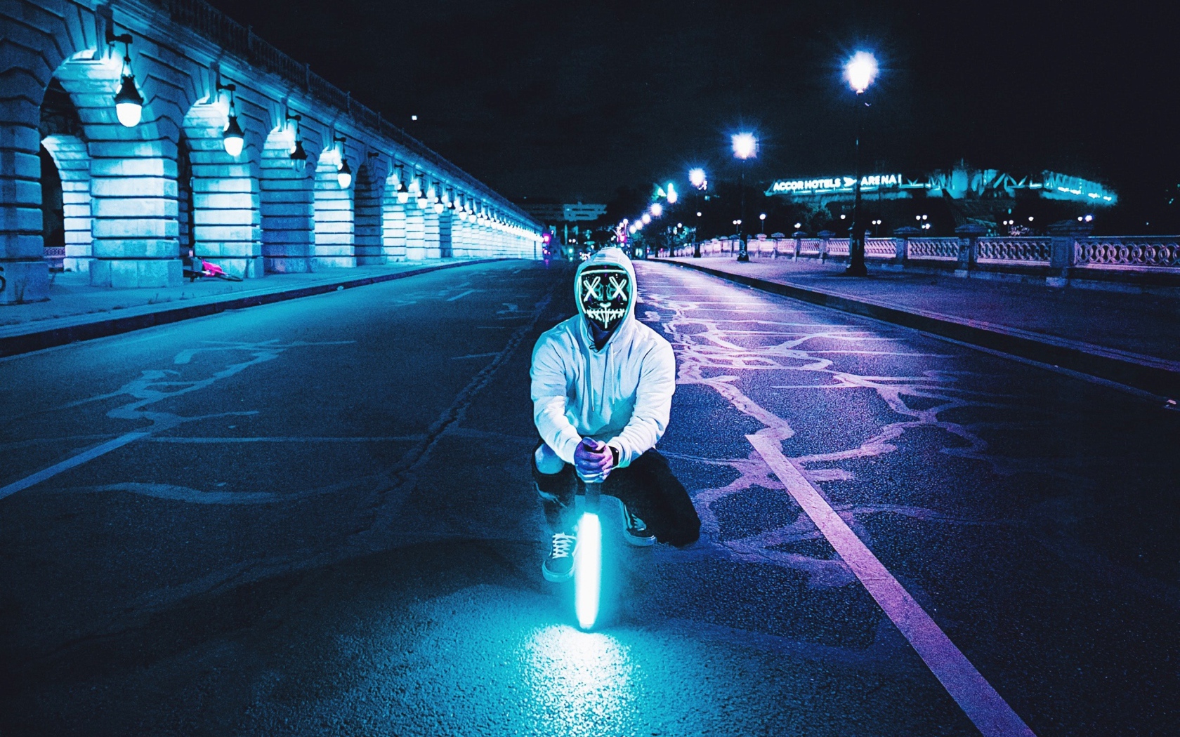 Парень в светящейся маске сидит с неоновой лампой на дороге