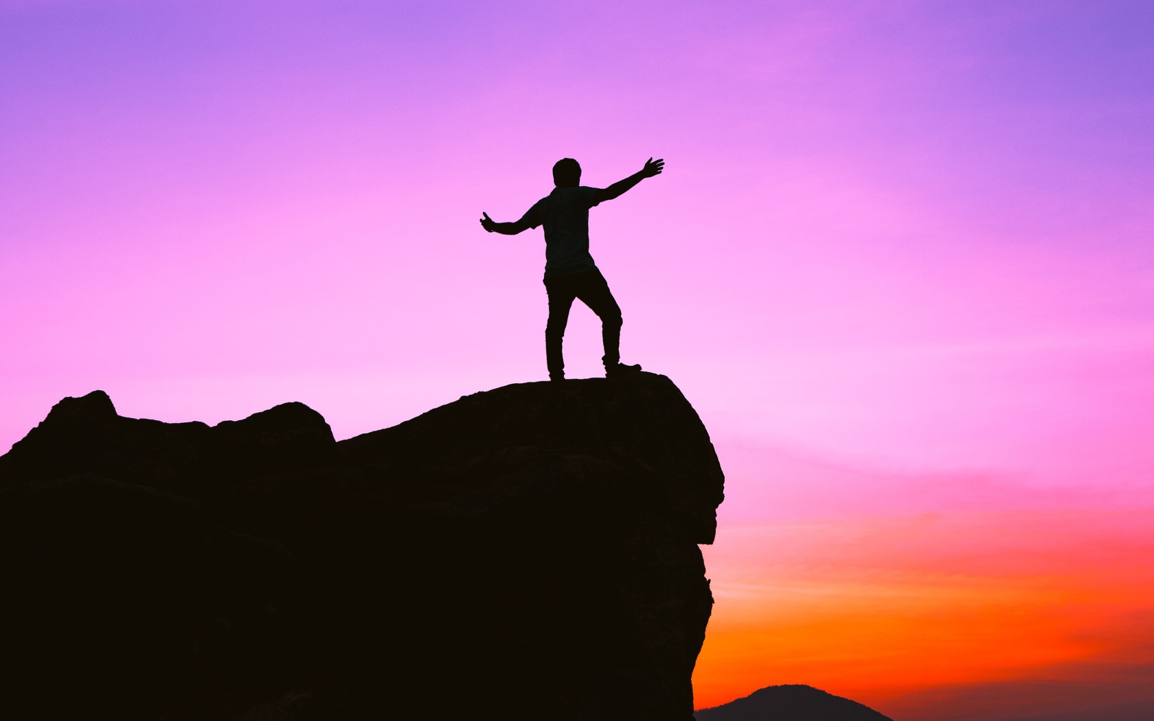 Мужчина стоит на краю утеса на закате