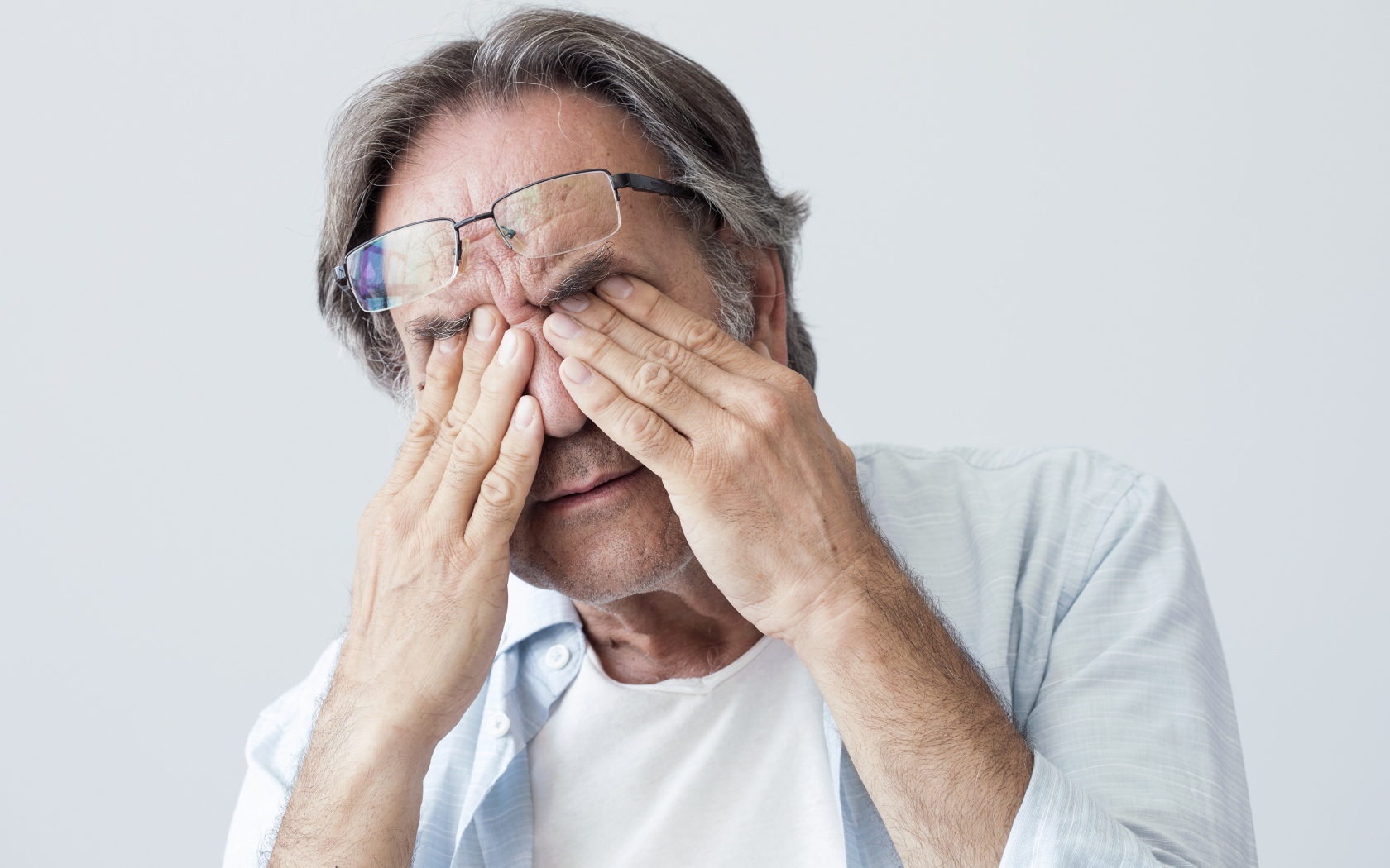 Пожилой мужчина трет глаза на сером фоне
