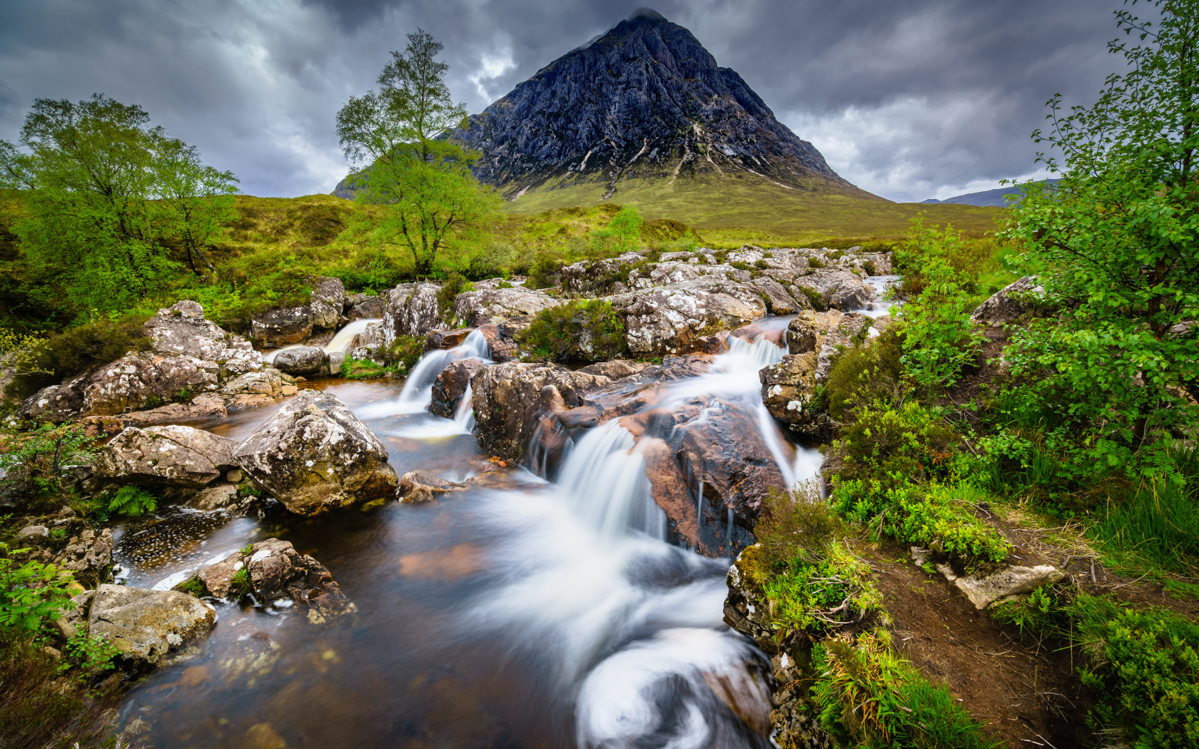 Быстрая вода в реке на фоне высокой горы под грозовым небом 