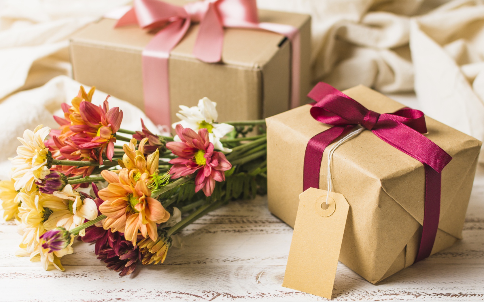 Букет разноцветных хризантем с подарками на столе 