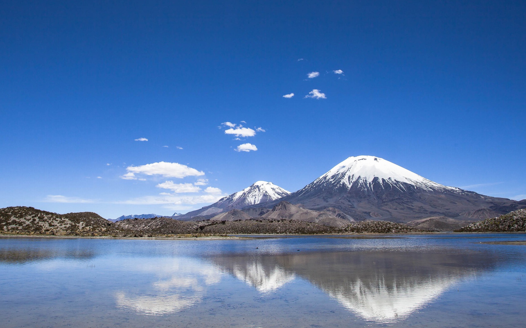 Заснеженные вершины гор под голубым небом отражаются в воде 