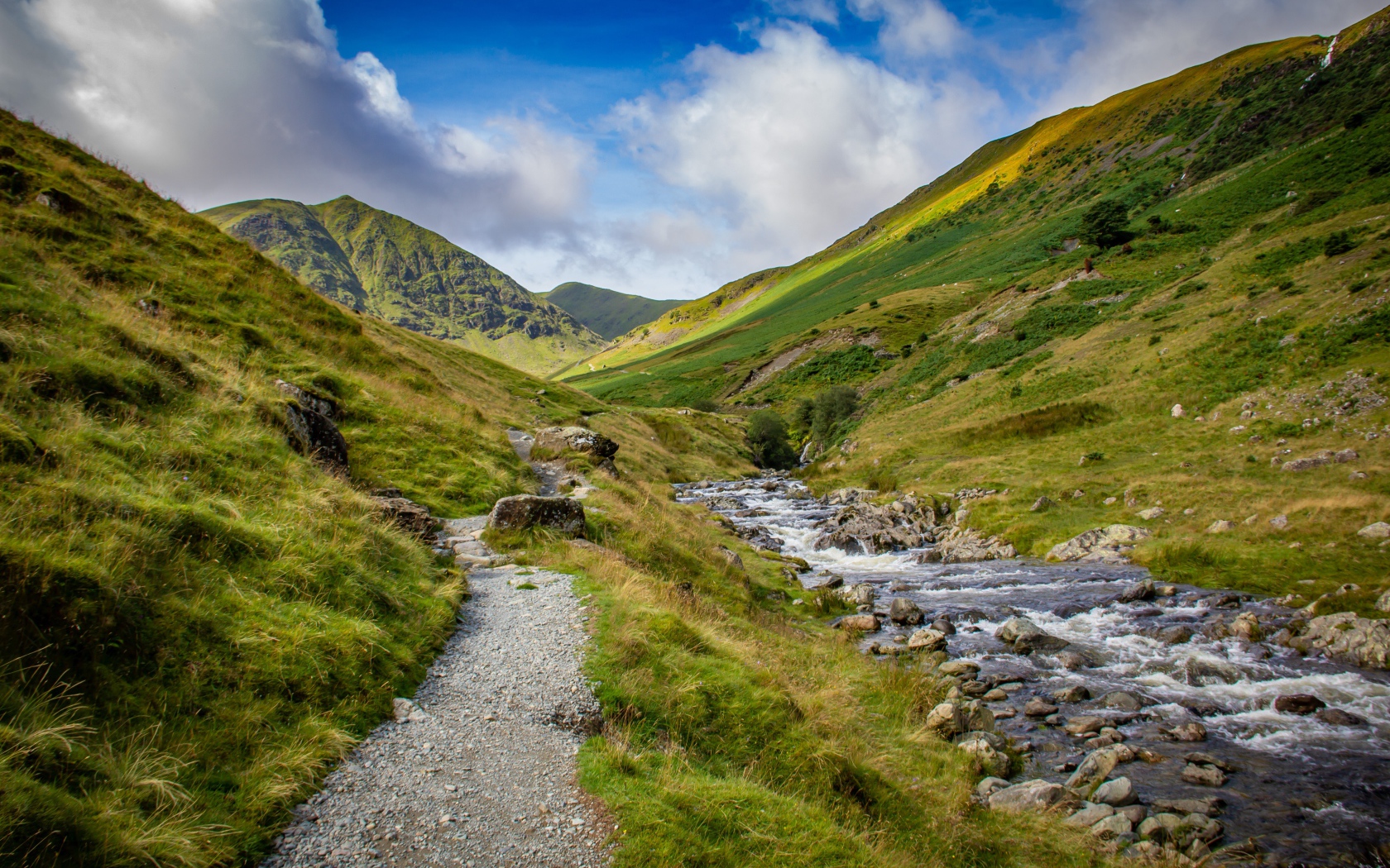 Тропа у реки на фоне покрытых зеленью гор 