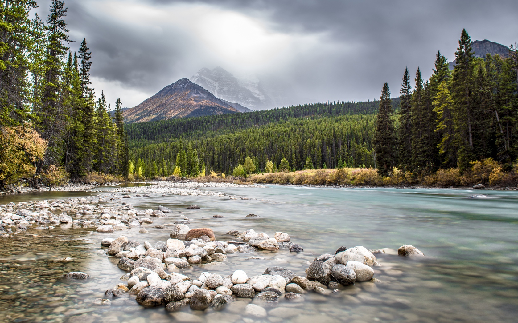 Много камней в реке на фоне гор и хвойного леса