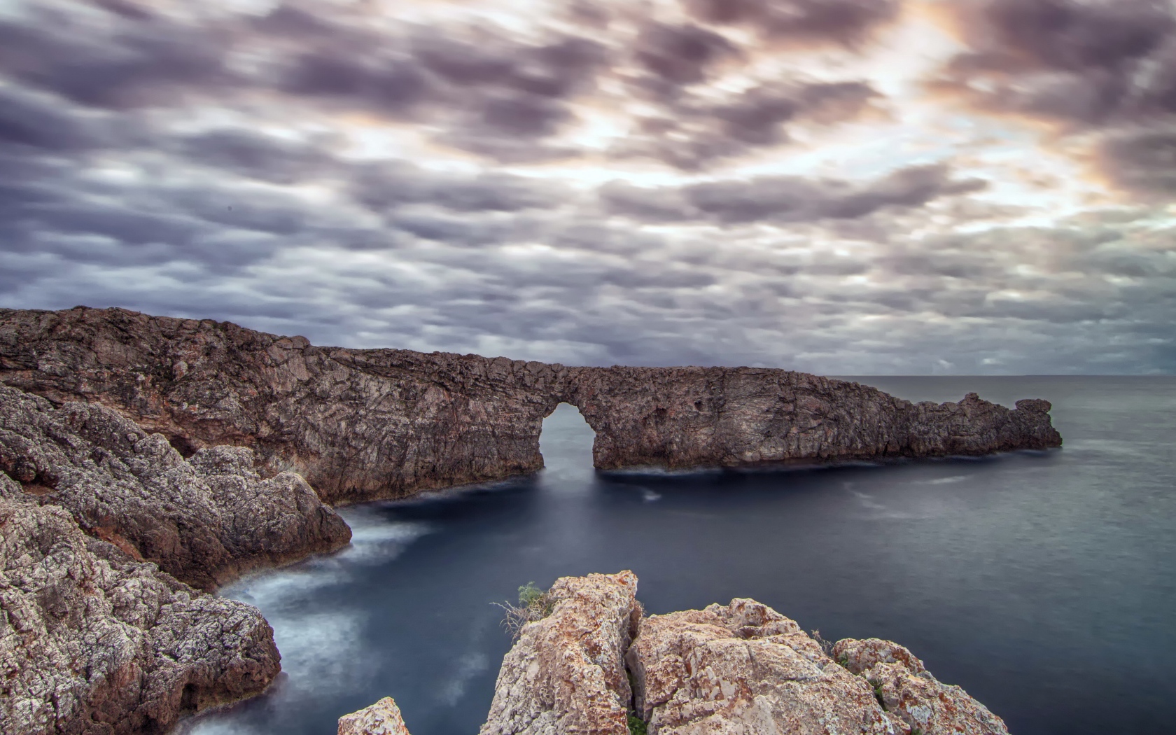 Арка в скале в море под пасмурным небом 